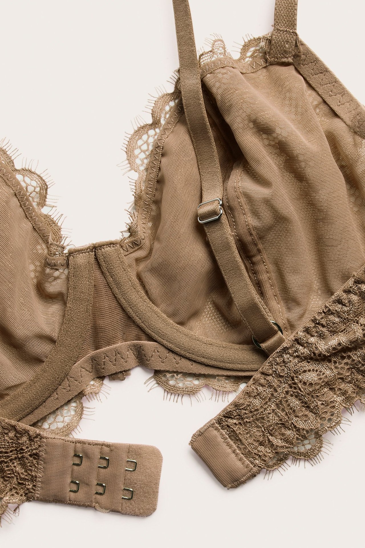 Zbliżenie beżowego, nieusztywnianego biustonosza z fiszbinami, z koronki, błyszczącymi ramiączkami i zapięciem.