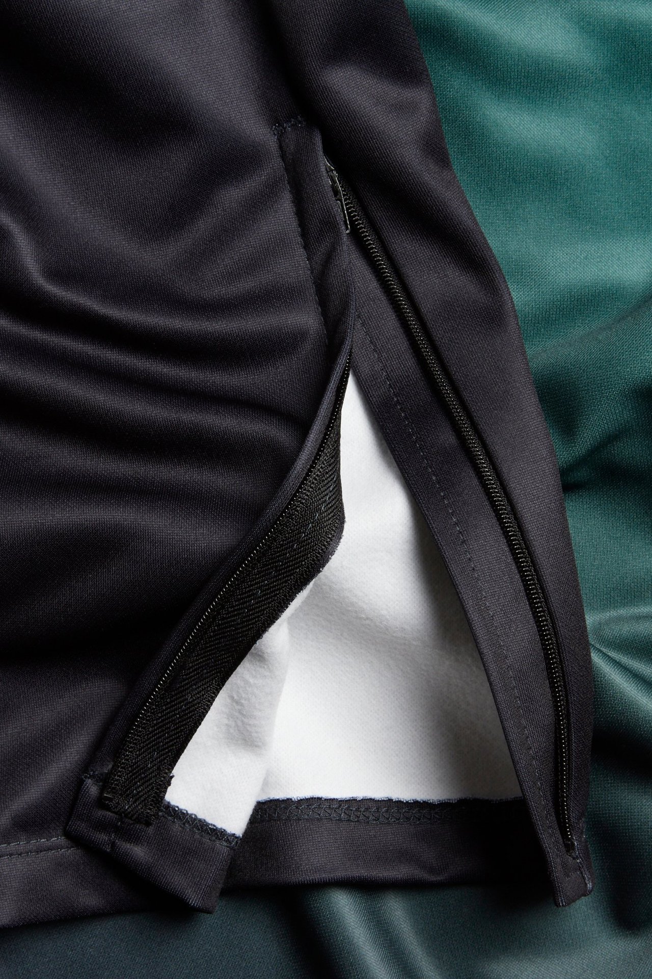 Zbliżenie czarnych spodni dresowych z otwartym zamkiem błyskawicznym u dołu, ukazującym białą podszewkę z polaru.