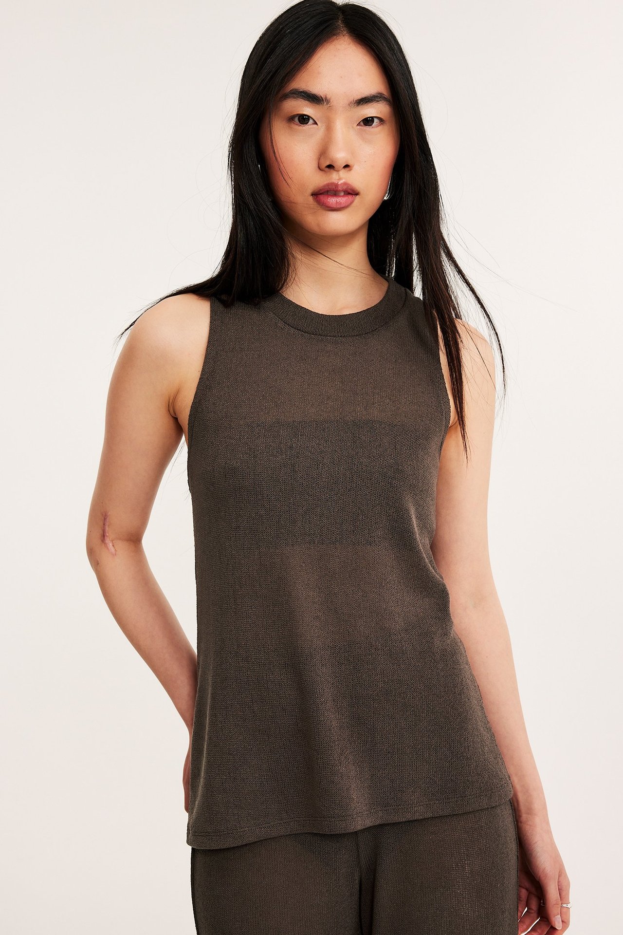 Forfra, kvinne i mørkebrun strukturert ermeløs topp med matchende bukser.