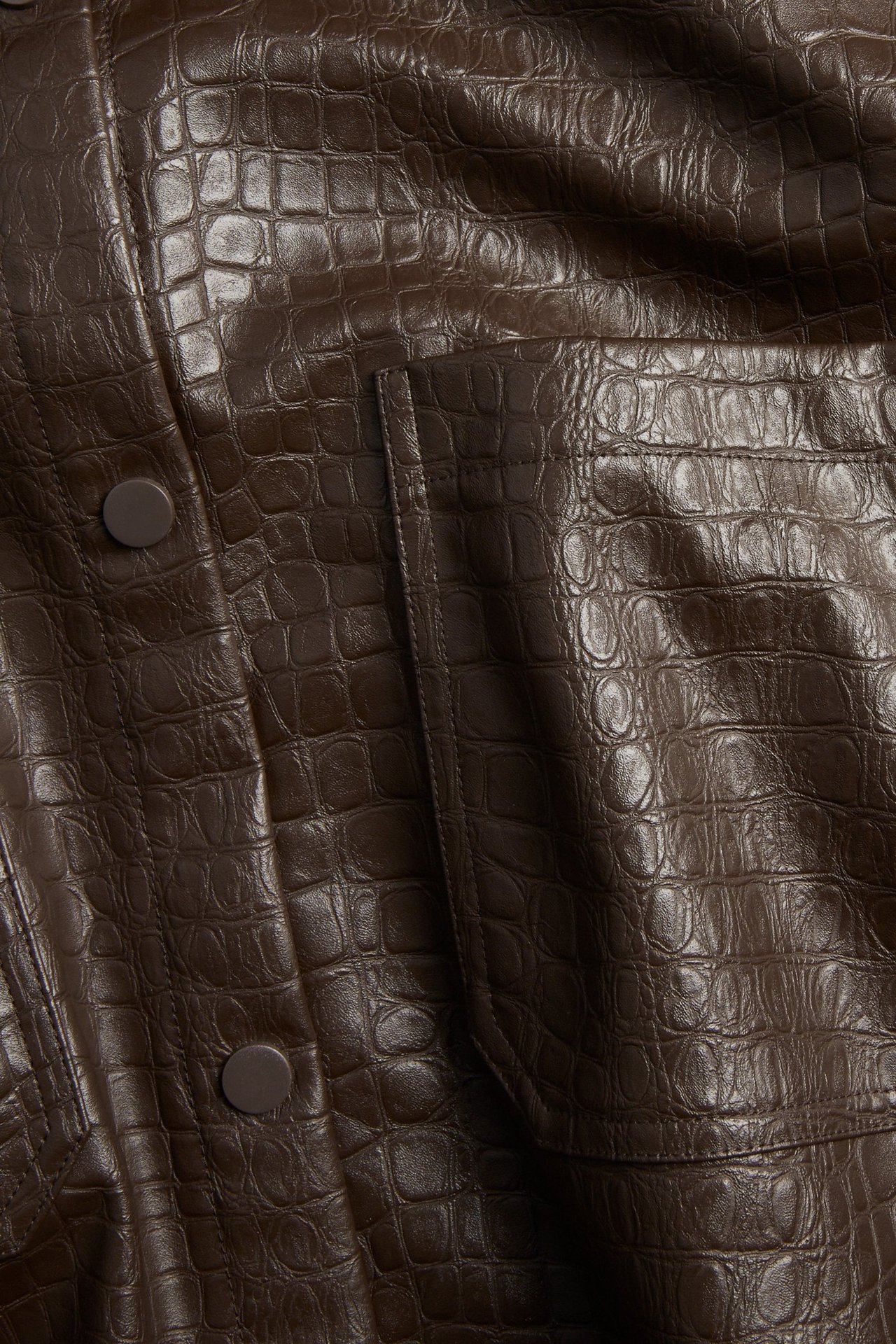 Zbliżenie na ciemnobrązową koszulę ze sztucznej skóry z wytłoczeniem krokodyla, z kieszeniami i guzikami.