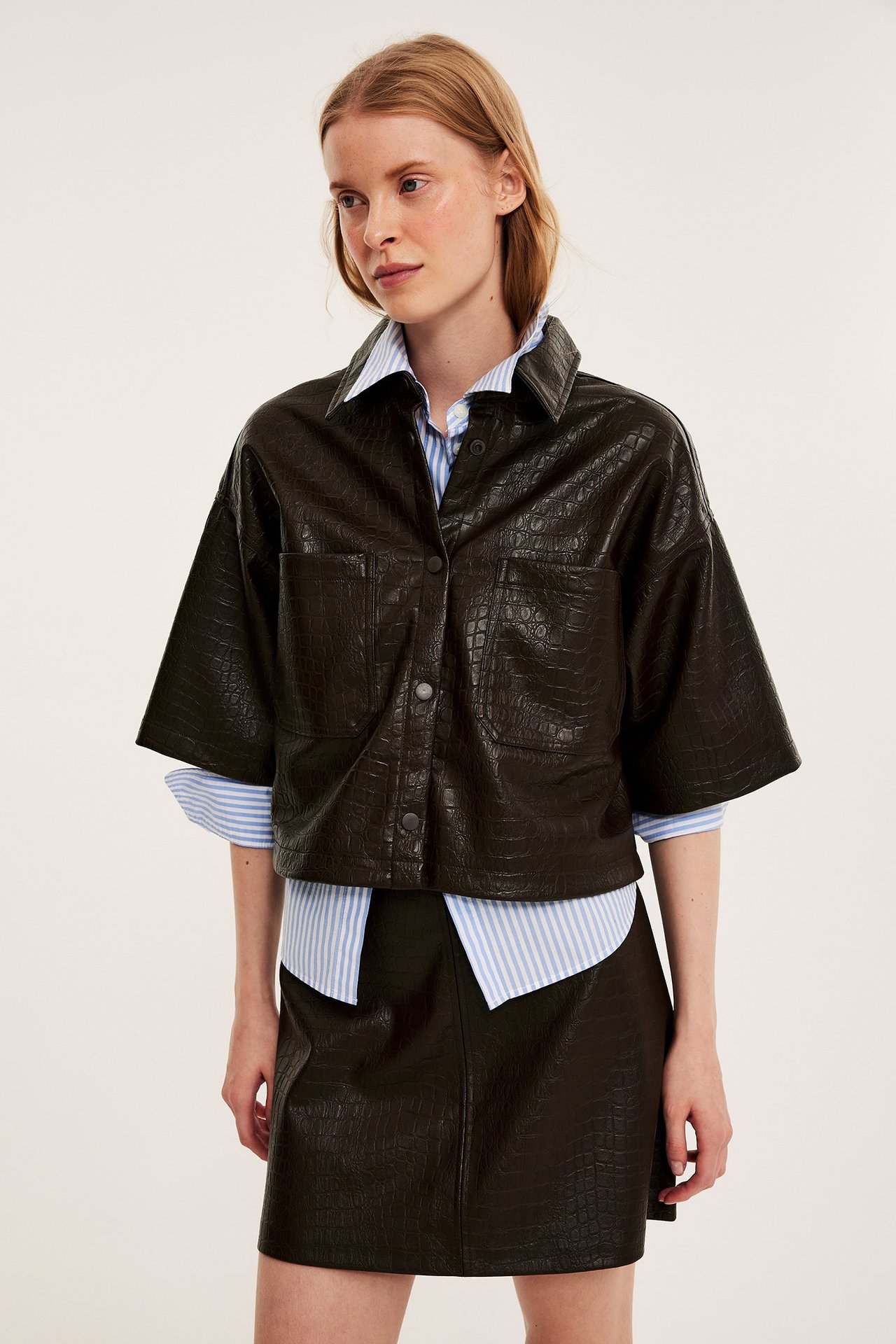 Etunäkymä: Nainen tummanruskeassa kuvioidussa tekonahkapaidassa, raidallisessa paidassa ja yhteensopivassa hameessa.