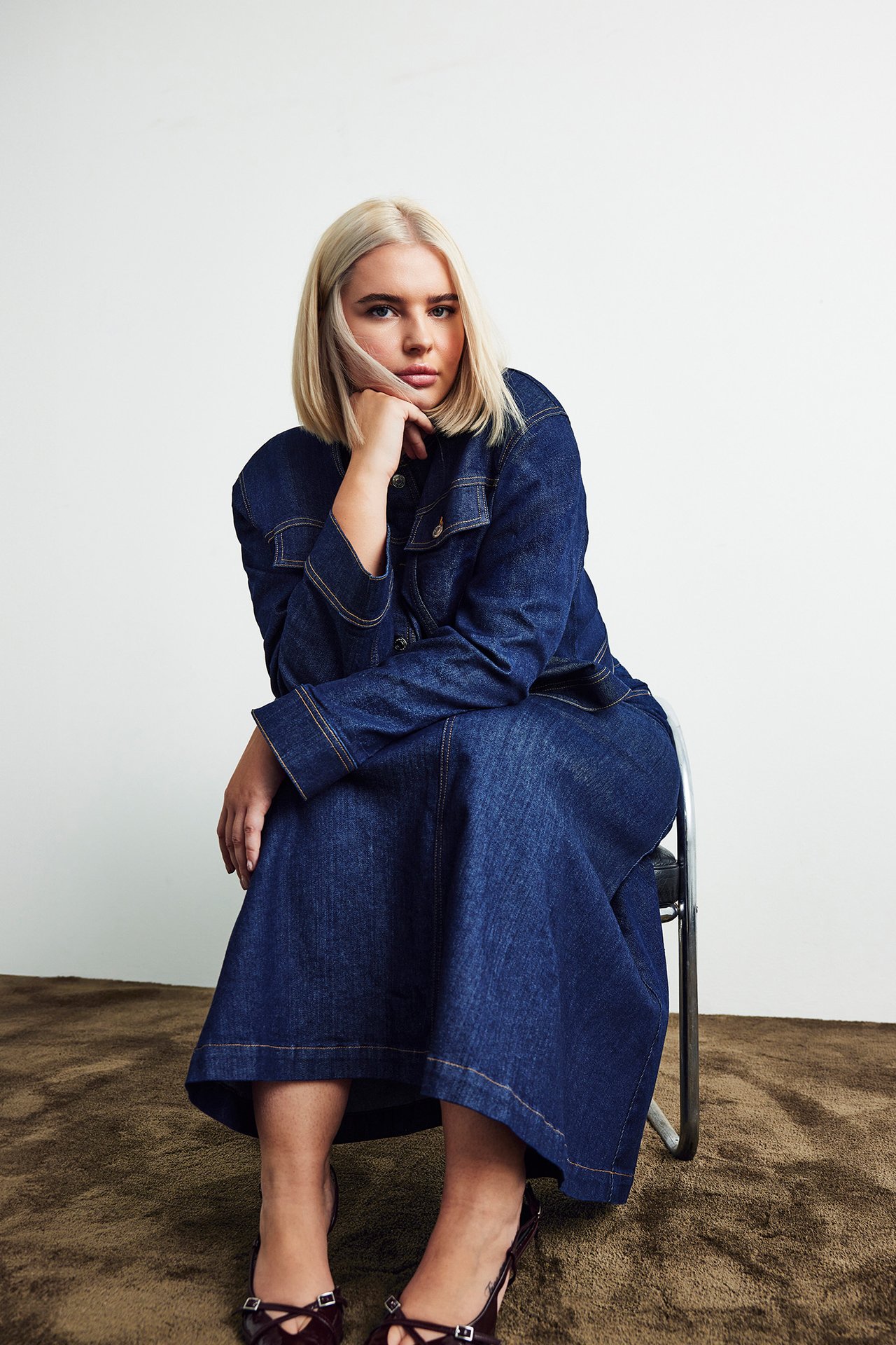 Edestä: Nainen yllään tumma farkkutakki ja yhteensopiva pitkä hame, punaruskeilla remmikoroilla.