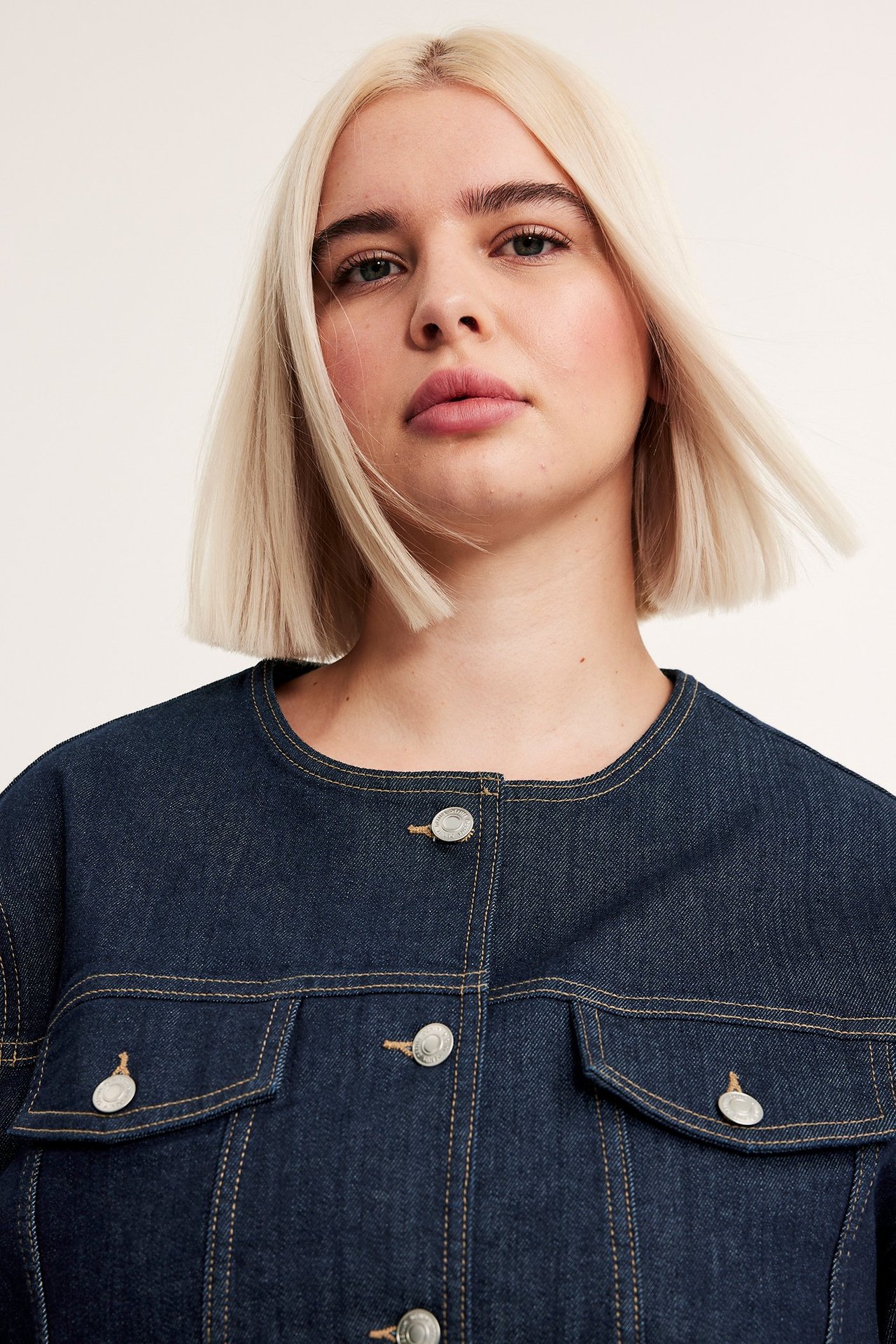 Lähikuva edestä naisesta yllään tumma denim lyhyt takki hopeanapeilla ja rintataskuilla.