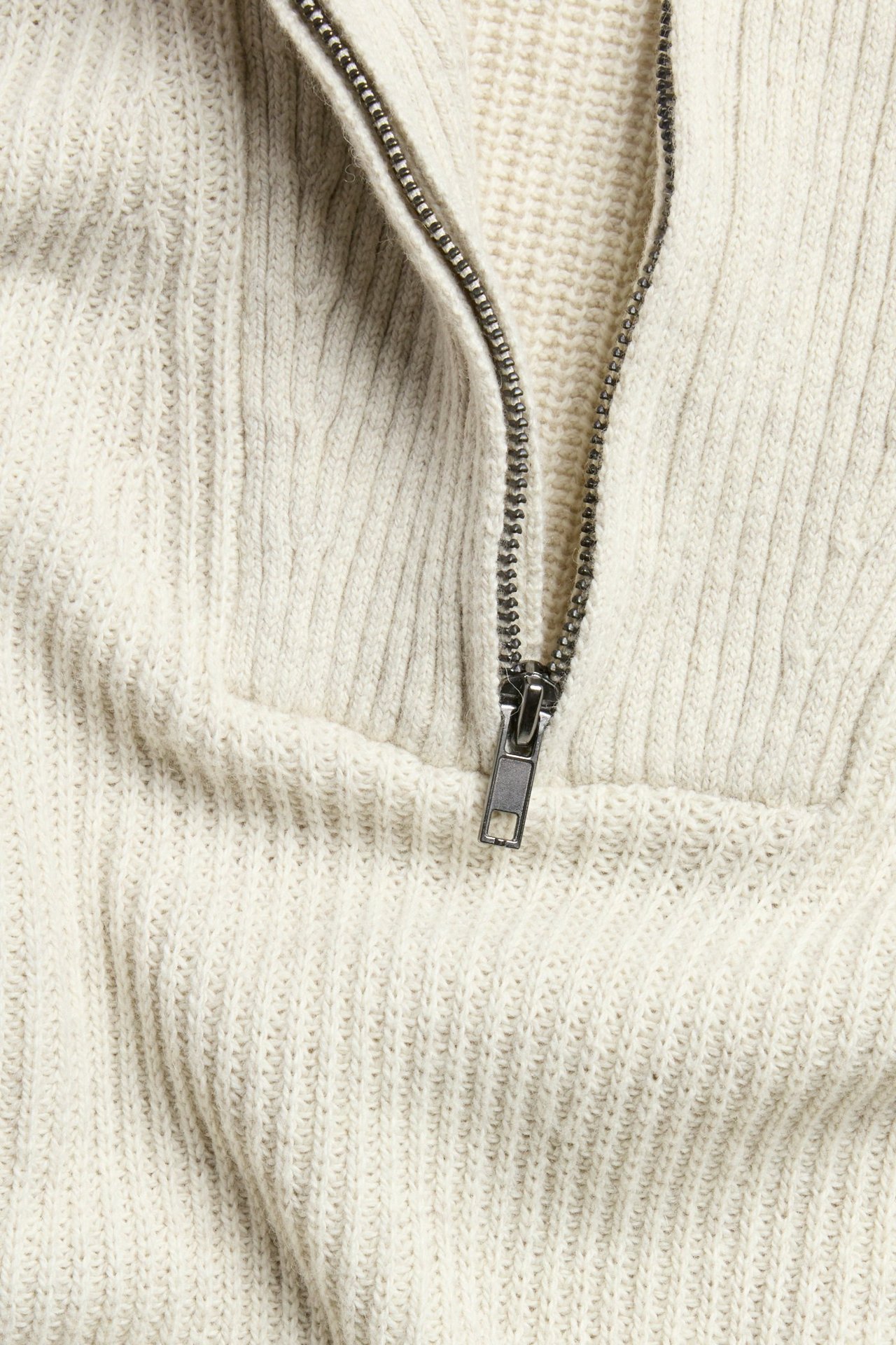 Lähikuva beigestä meleeratusta neulotusta half-zip-neuleesta tummalla vetoketjulla.