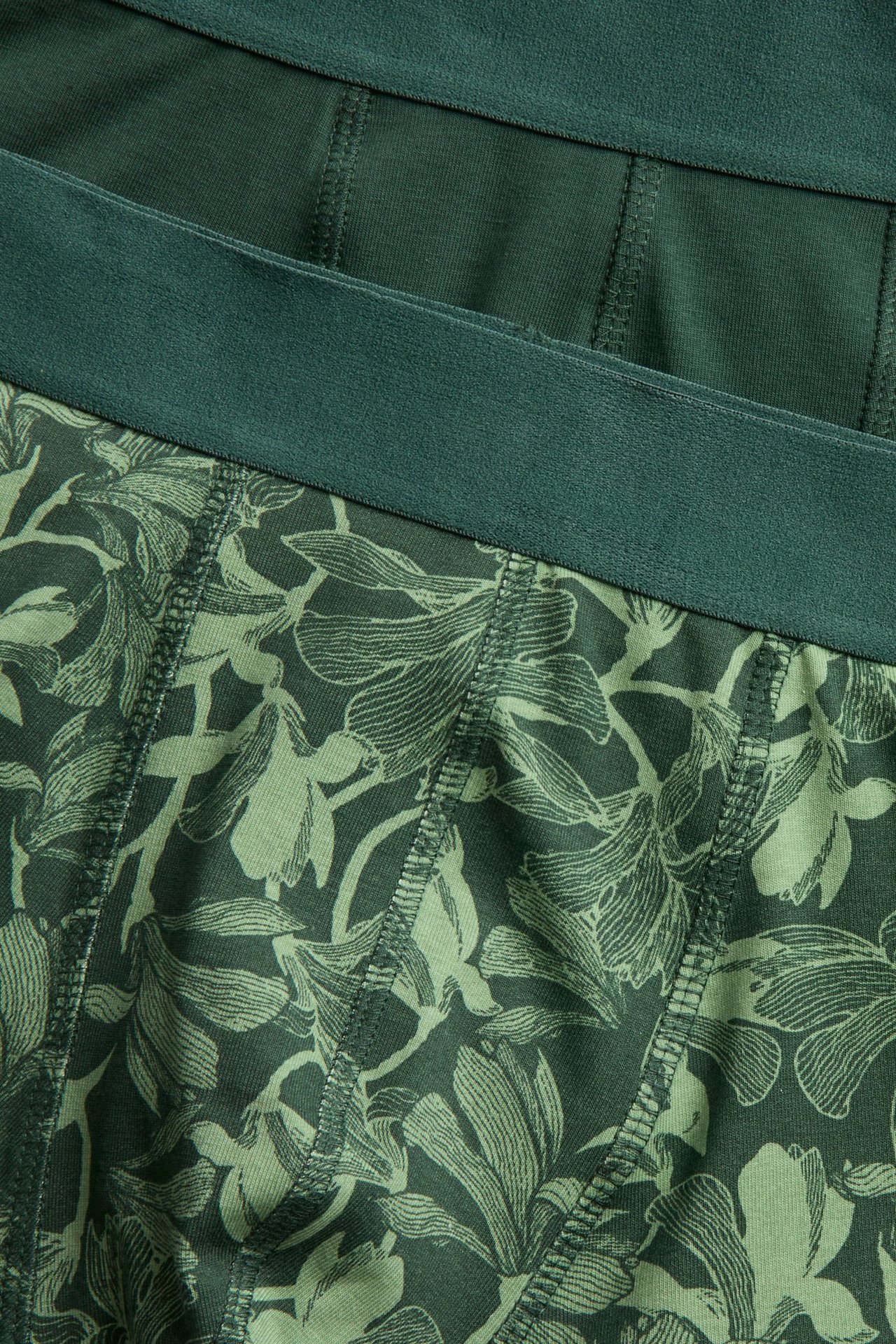 Lähikuva tummanvihreistä kukkakuvioisista boksereista ja yksivärisistä tummanvihreistä boksereista.