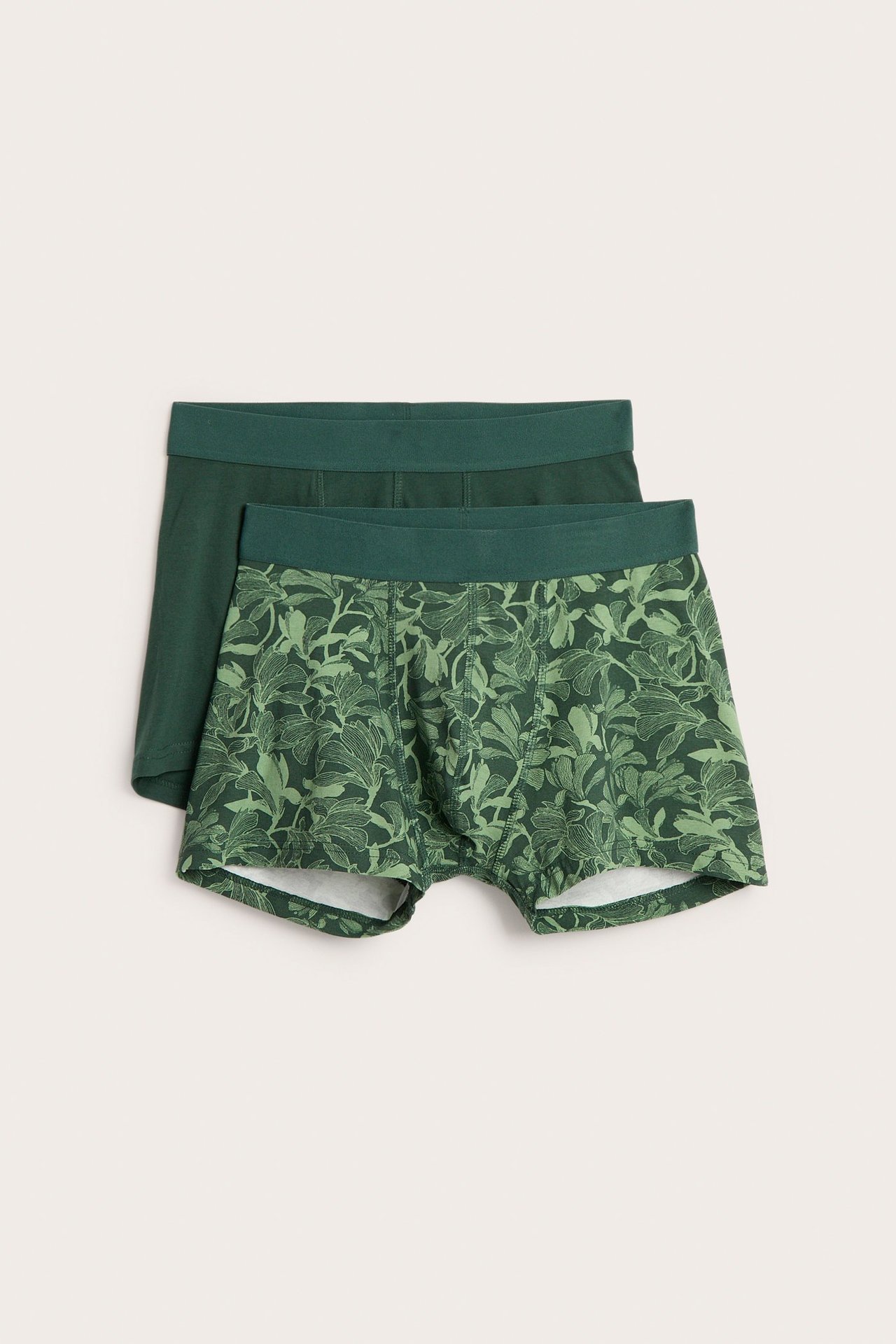Edestä näkymä kahdesta miesten bokserista: toinen vihreä lehtikuviolla, toinen yksivärinen tummanvihreä. Molemmat puuvilla-elastaania.