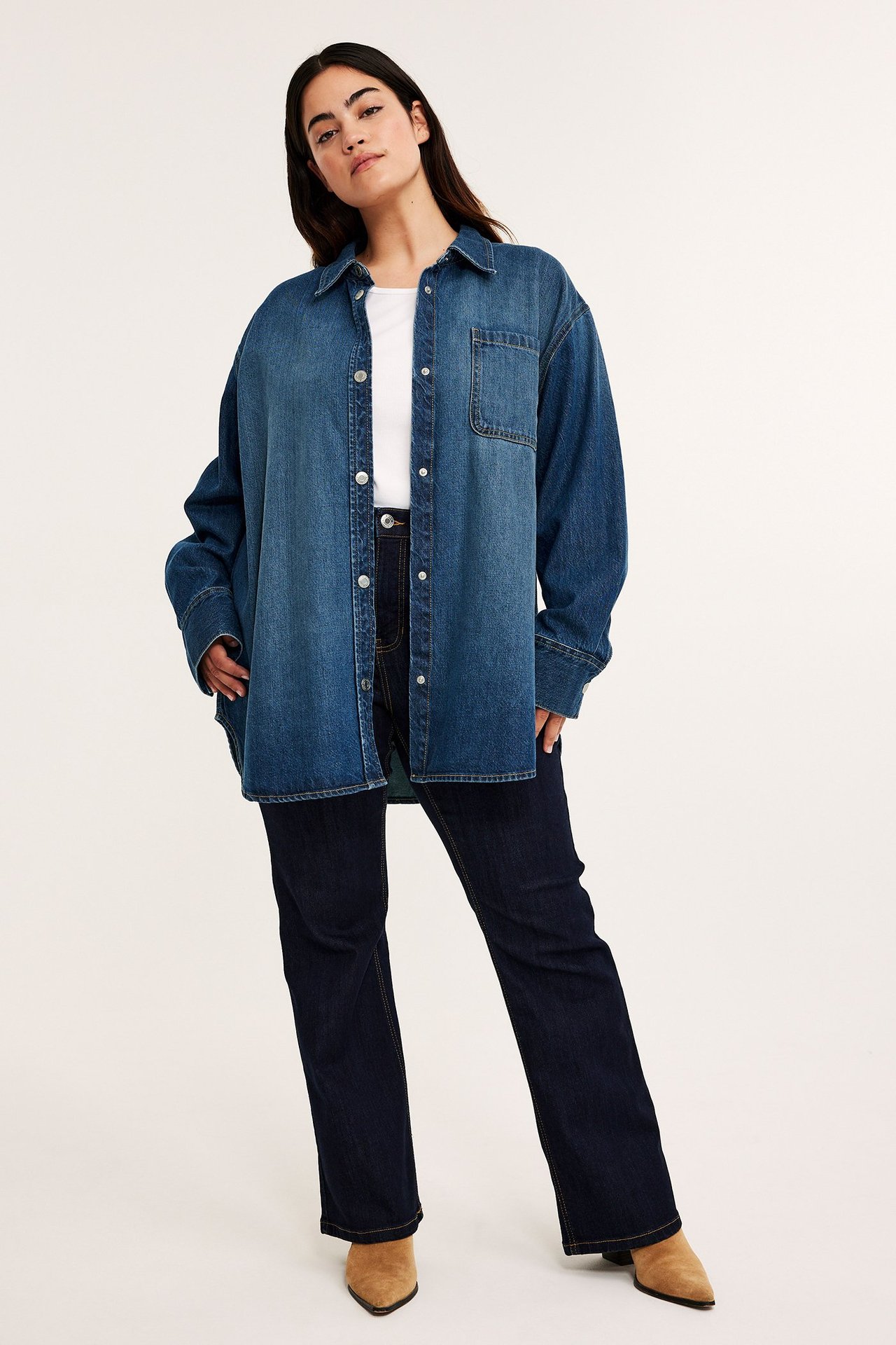 Etunäkymä: Nainen ylisuuressa sinisessä farkkupaidassa, valkoisessa t-paidassa, tummansinisissä farkuissa ja ruskeissa saappaissa.