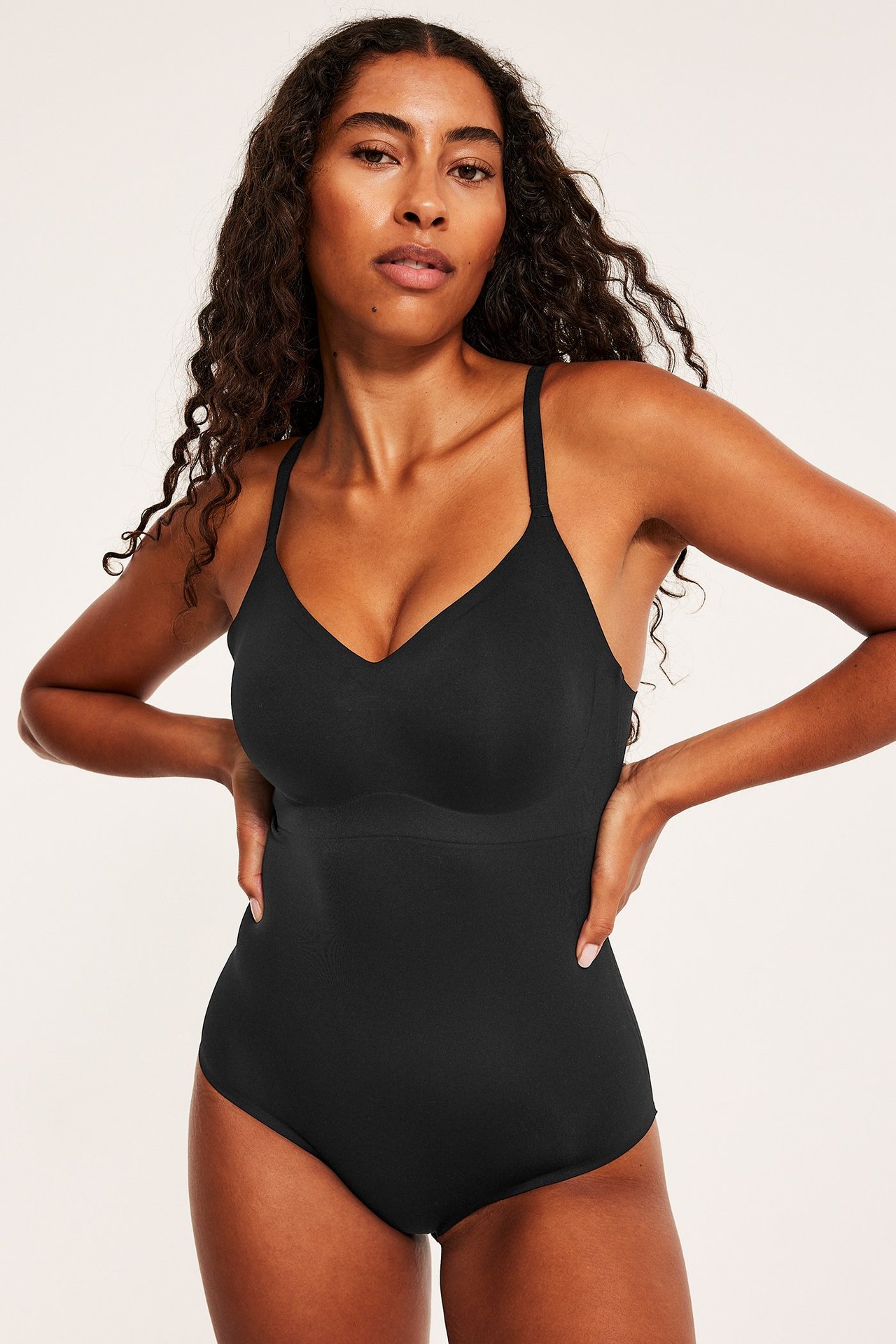 Edestä kuvattu nainen yllään musta pehmeä body säädettävillä olkaimilla ja topatuilla kupeilla.