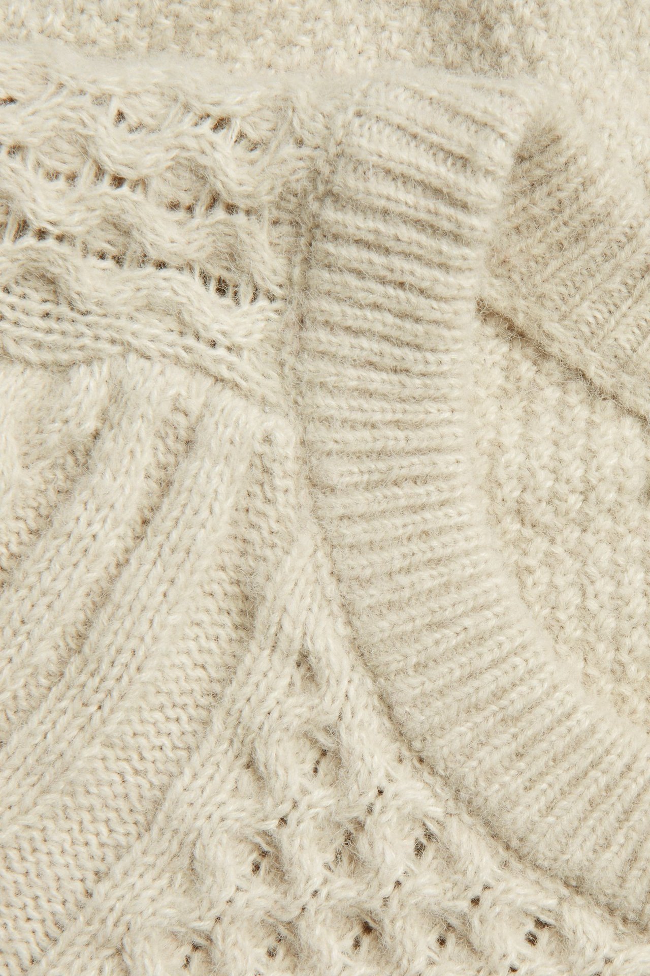 Zbliżenie jasnobeżowego swetra z warkoczowym splotem i okrągłym dekoltem.