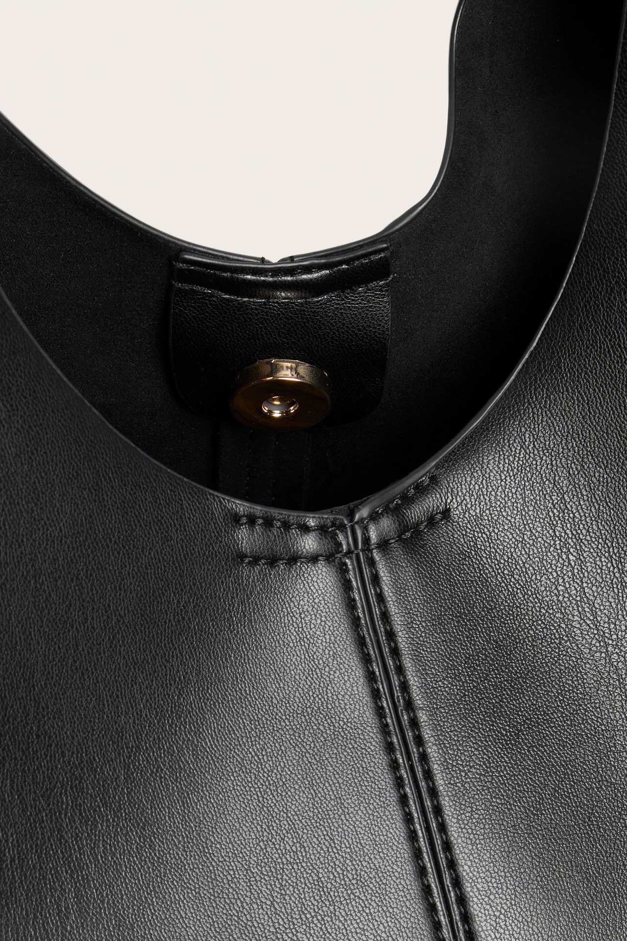 Zbliżenie czarnej torebki ze sztucznej skóry ze złotym zapięciem magnetycznym i widocznymi szwami.