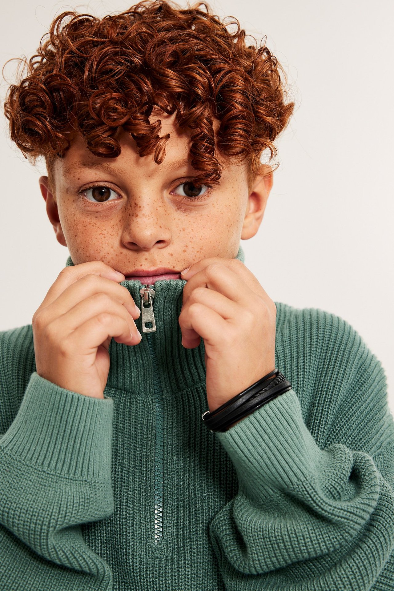 Dziecko w khaki zielonym swetrze z półzamkiem, podwinięte rękawy.