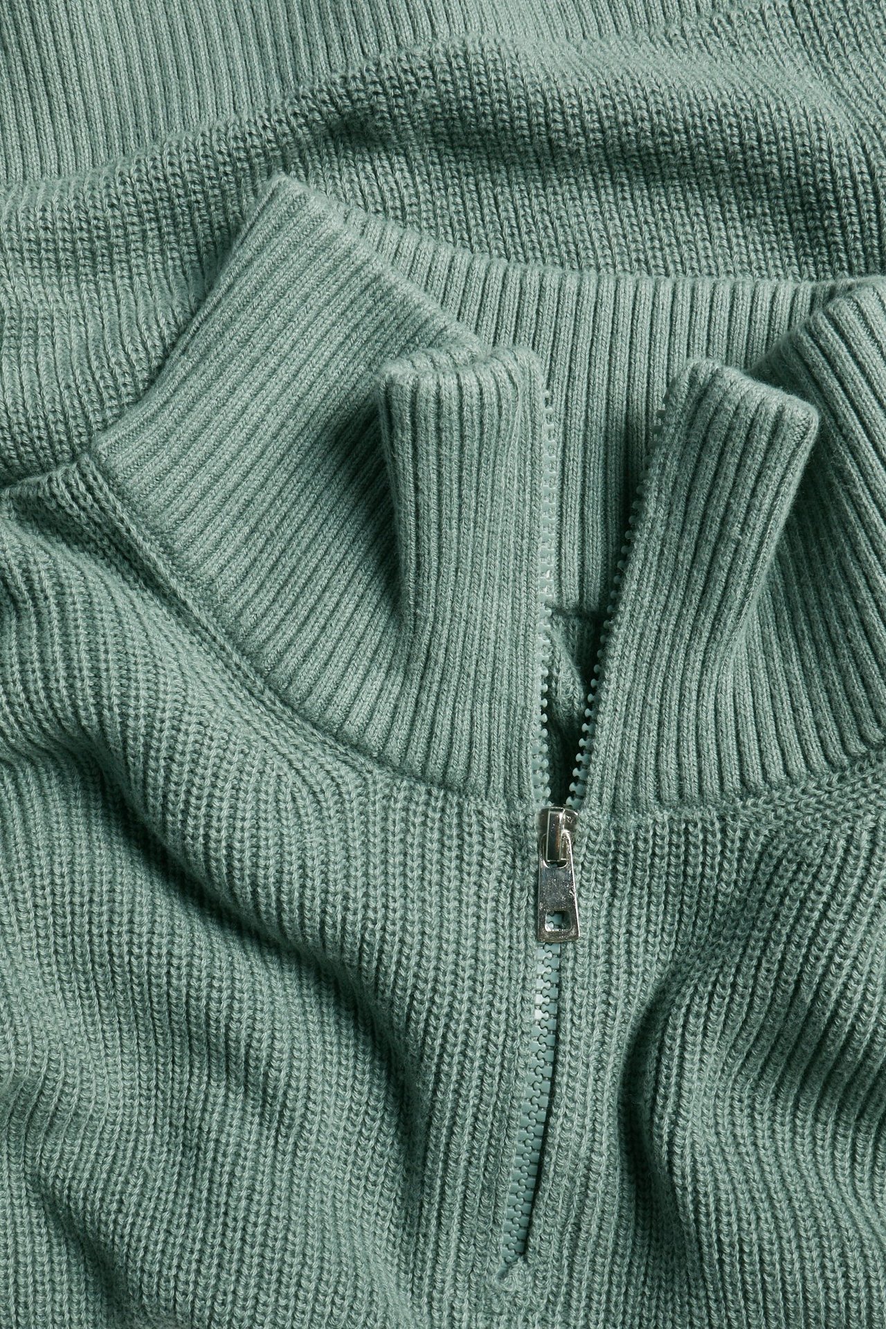 Zbliżenie na khaki zielony prążkowany sweter bawełniany z półzamkiem i srebrnym zamkiem błyskawicznym.