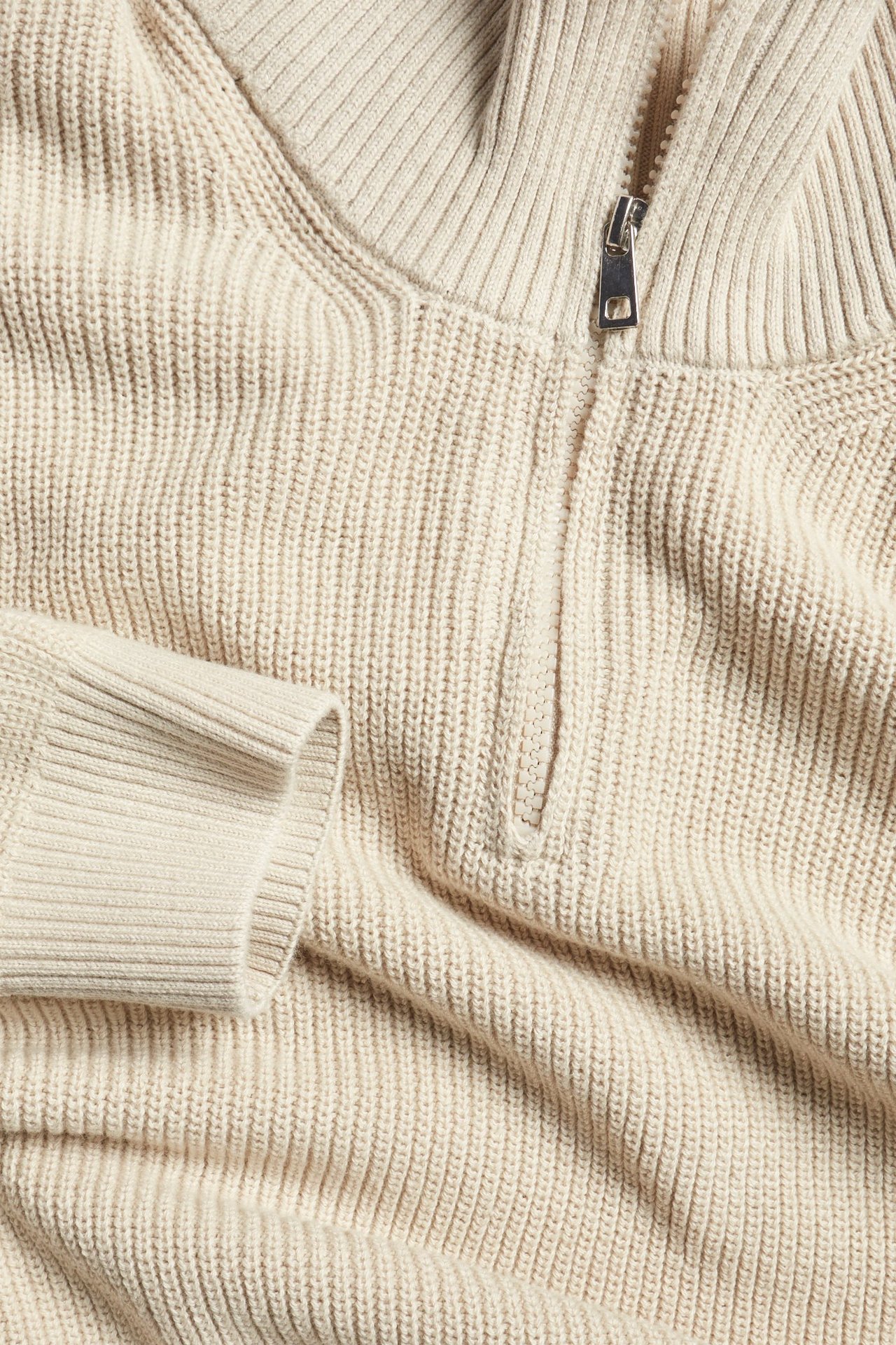 Zbliżenie beżowego, dzianinowego swetra bawełnianego z zamkiem błyskawicznym i prążkowaną fakturą.