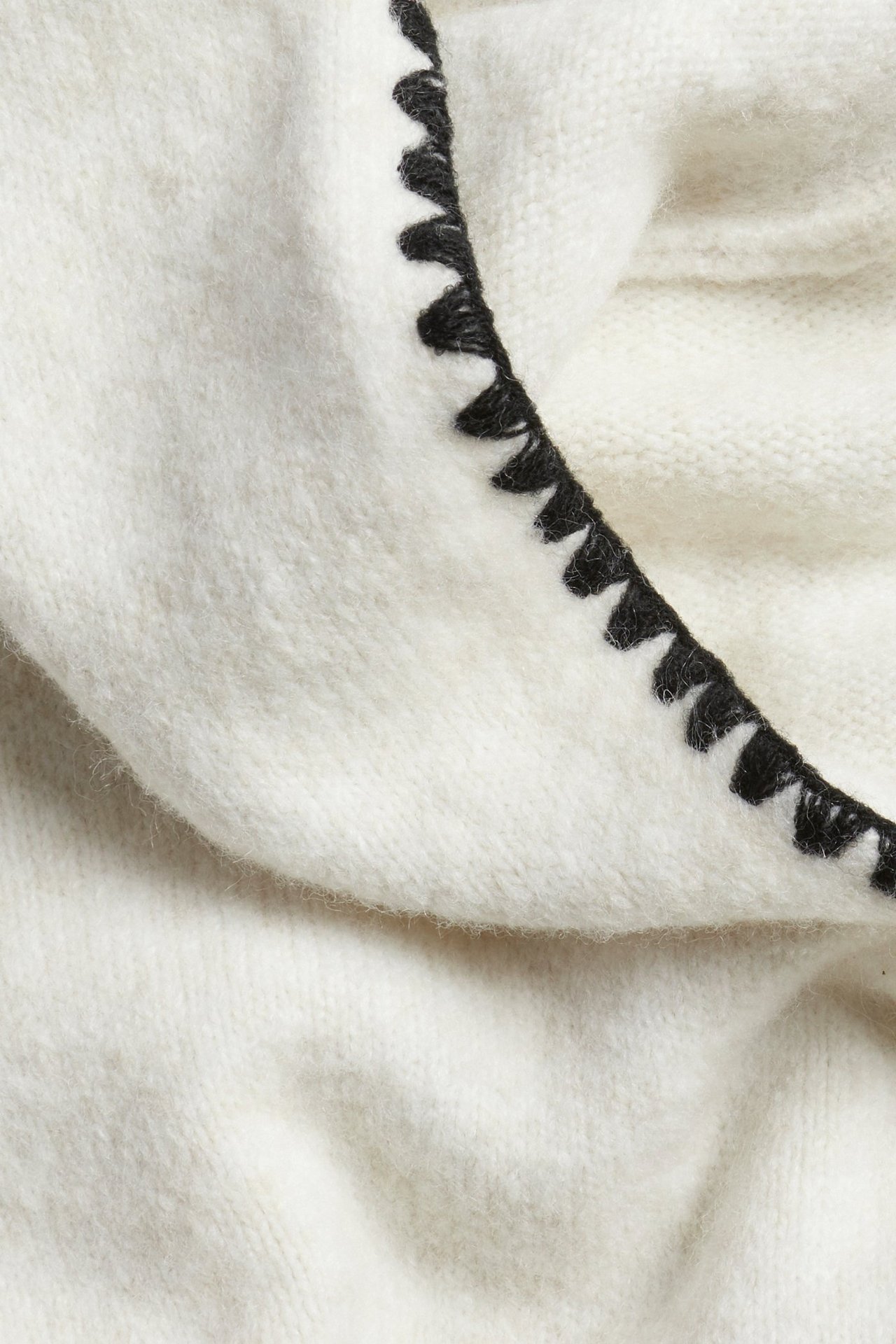 Zbliżenie białej melanżowej dzianinowej bluzy z kapturem z czarnymi ozdobnymi szwami wzdłuż otworu kaptura.