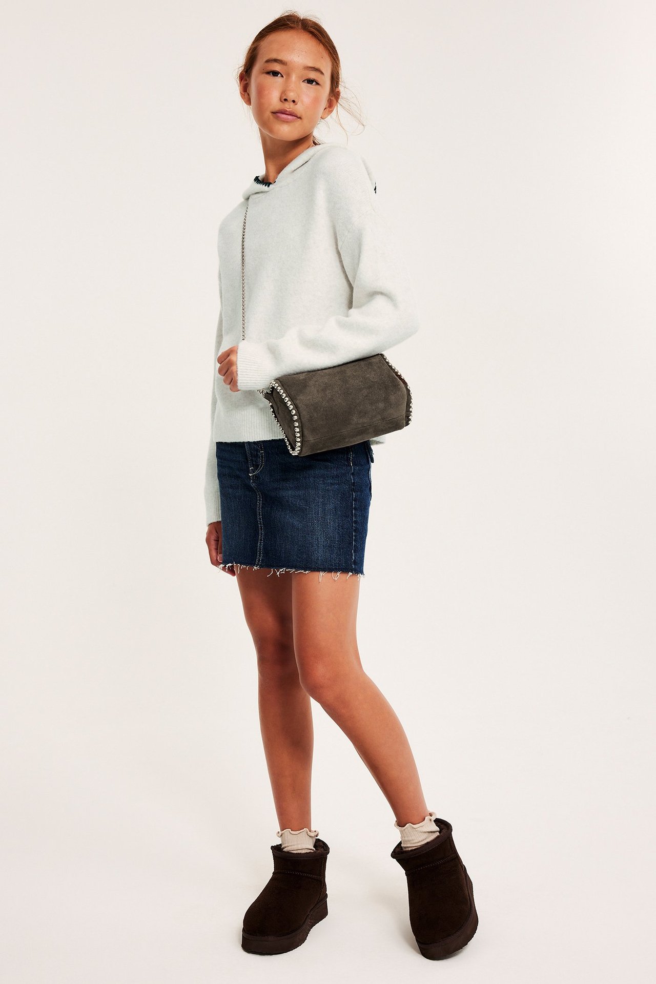 Widok z przodu: Dziecko w jasnoszarej melanżowej dzianinowej bluzie z kapturem, granatowej spódniczce i szarej torebce.