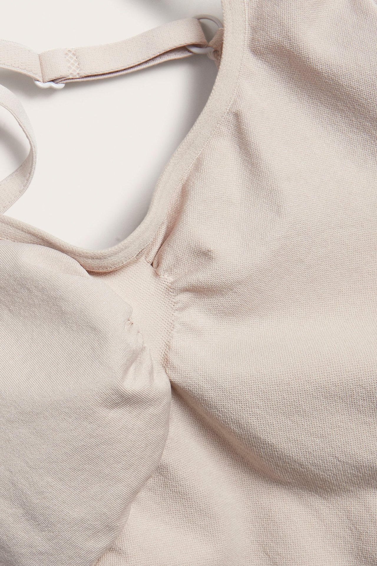 Zbliżenie beżowego, bezszwowego body modelującego z regulowanym ramiączkiem i marszczonym materiałem.