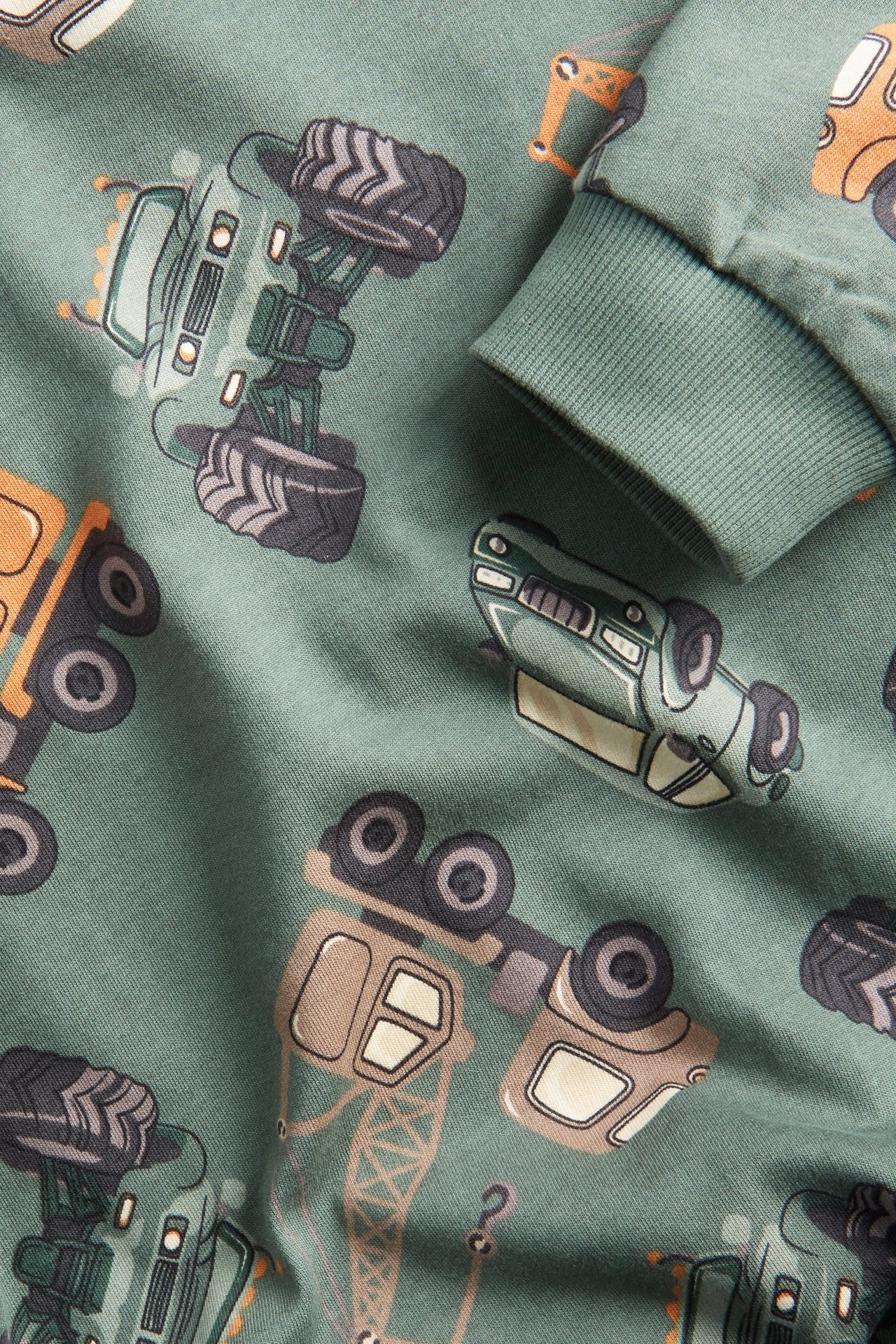 Zbliżenie na ciemnozieloną bawełnianą bluzę dziecięcą z wzorem pojazdów, widać ściągacz.