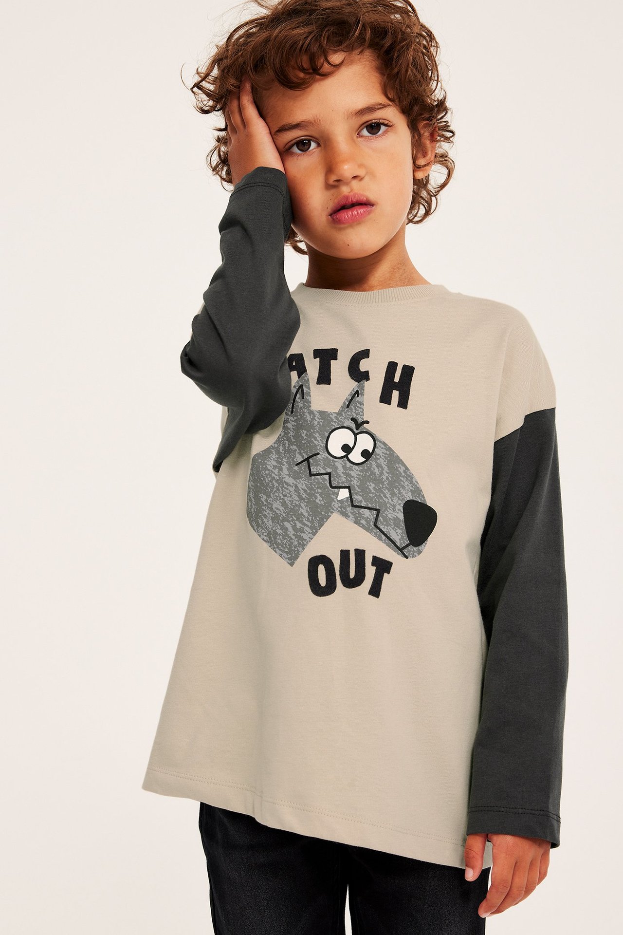 Widok z przodu: Dziecko w beżowej koszulce z długim rękawem, ciemnoszarymi rękawami i wilczym nadrukiem.