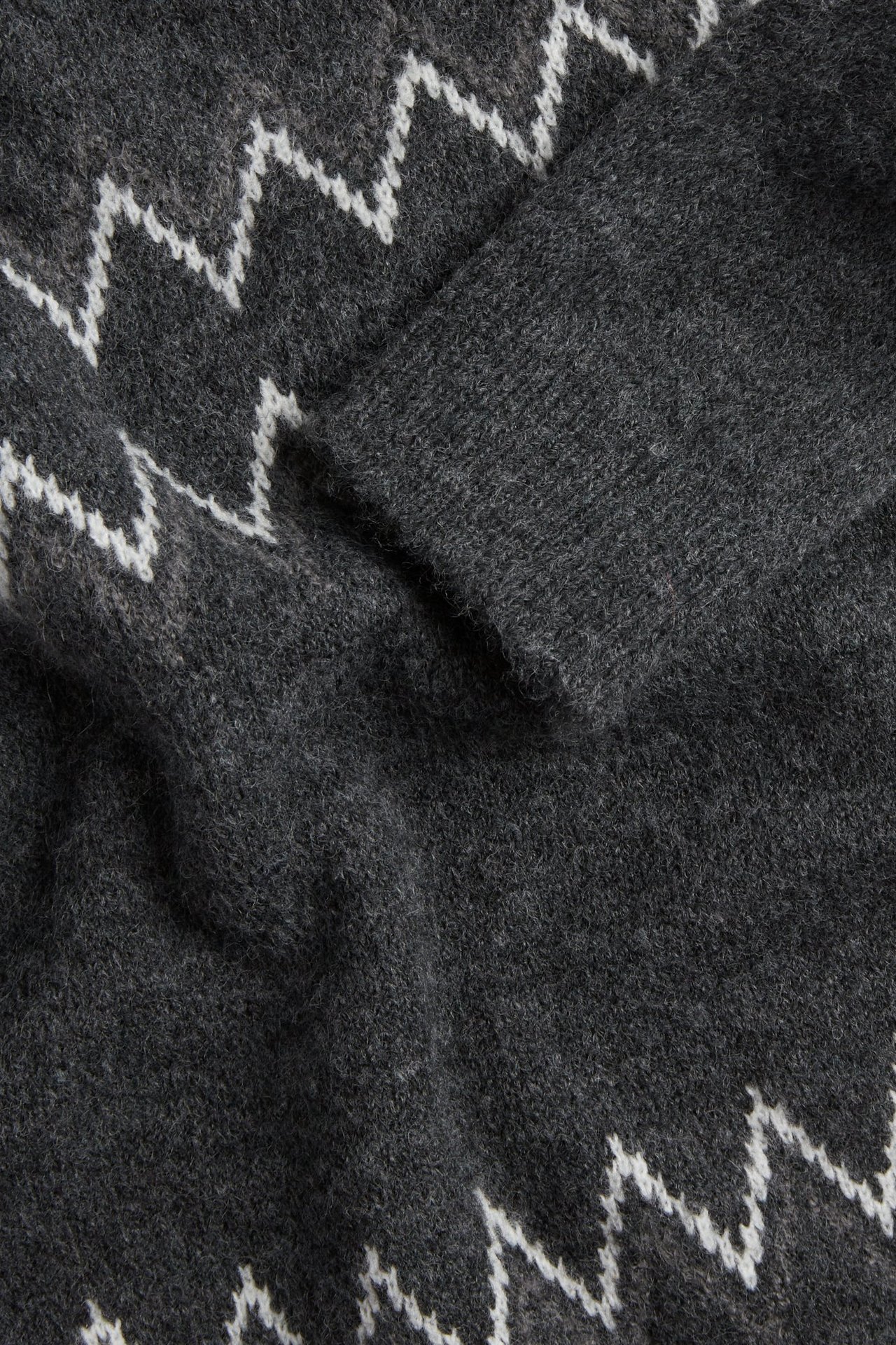 Närbild av en mörkgrå stickad tröja med vitt sicksack-mönster i jacquardväv.