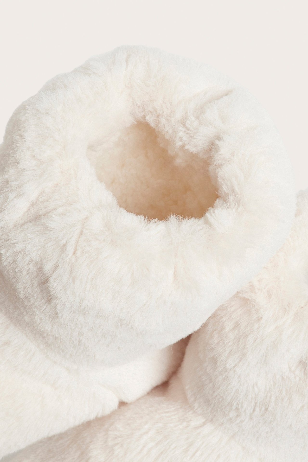 Nærbilde av en offwhite, myk boot-tøffel med fluffy pilefôr.