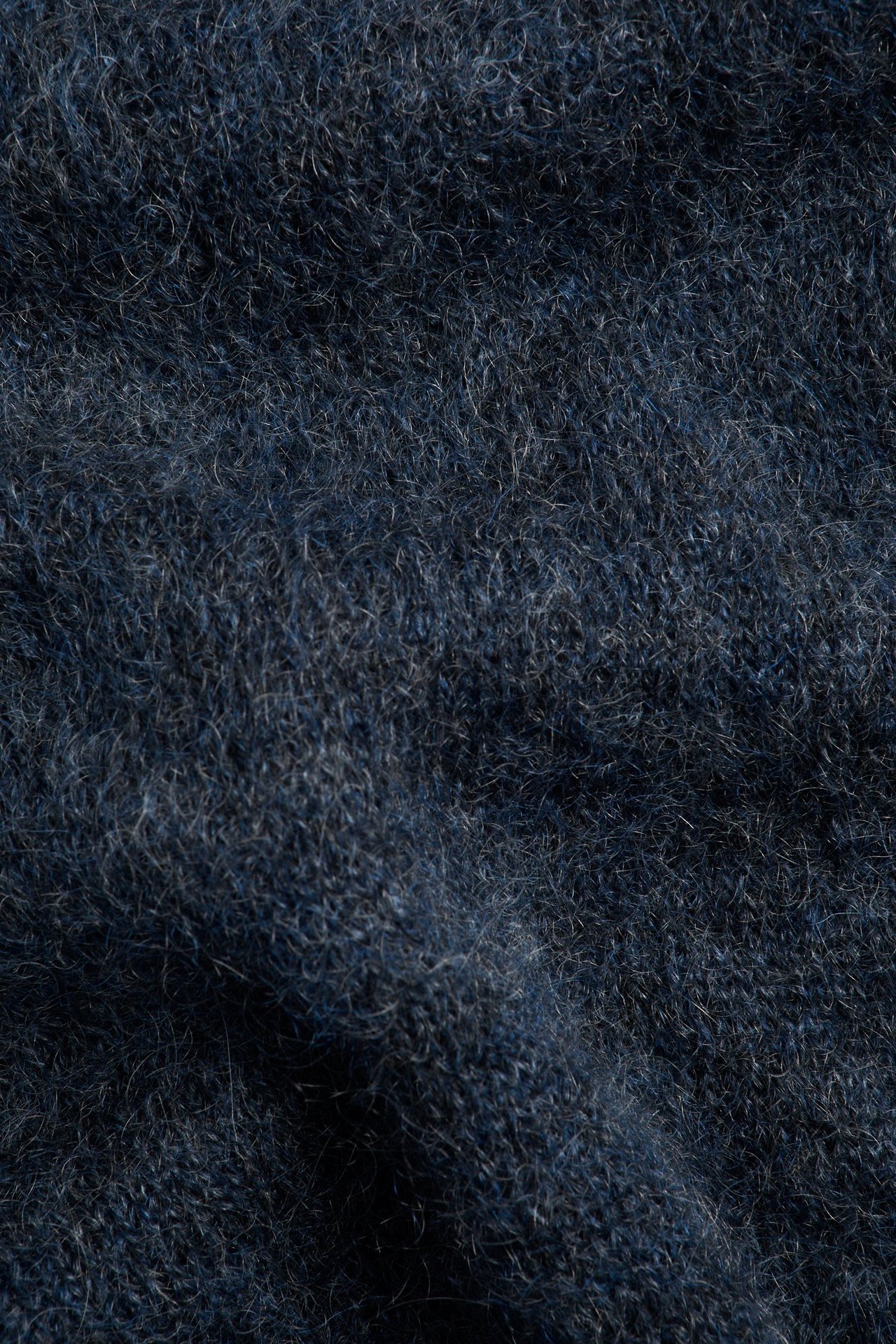 Zbliżenie na ciemnoniebieski sweter z dzianiny z domieszką moheru o puszystej fakturze.