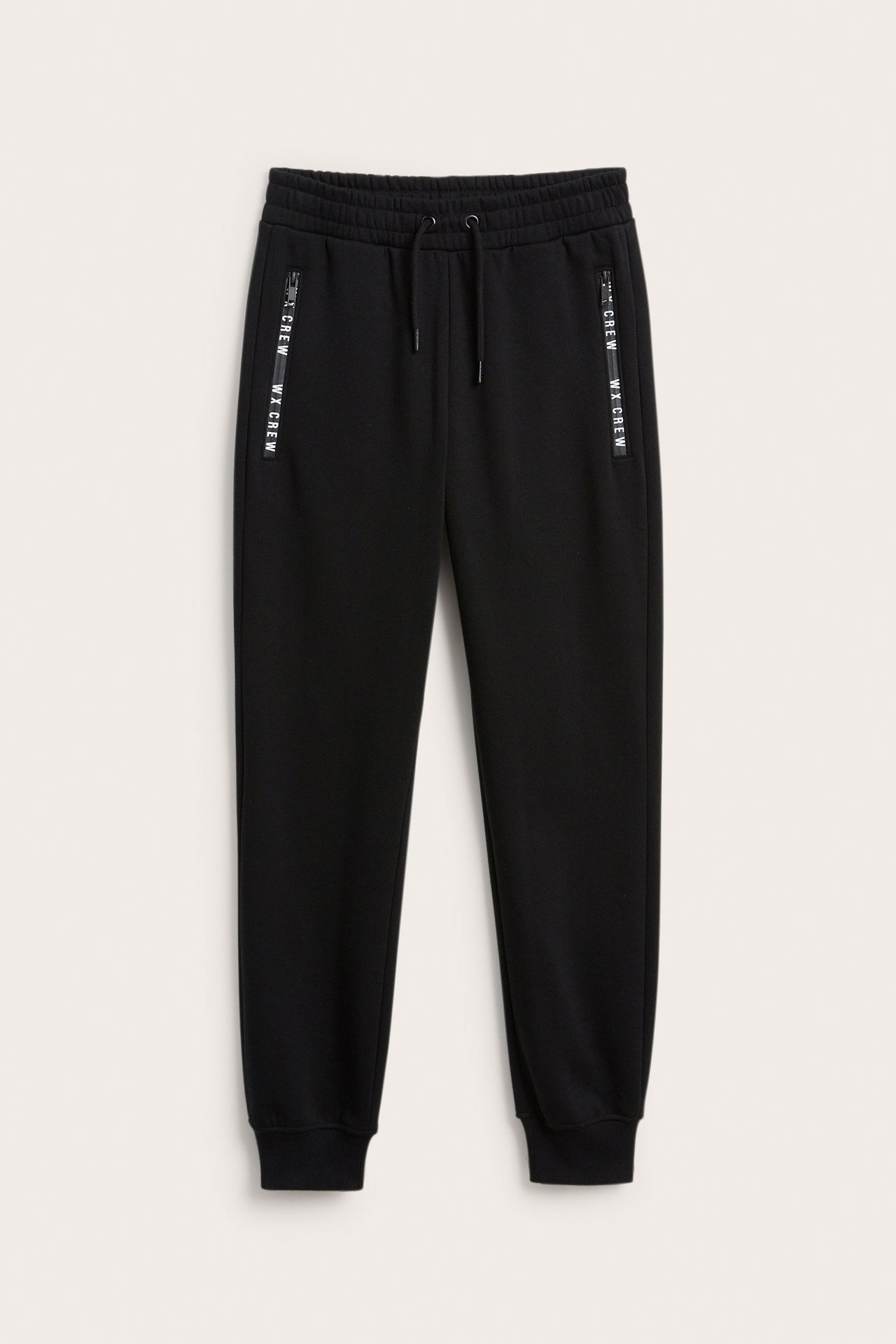 Widok z przodu czarnych dresów z bawełny, ze sznurkiem, bocznymi kieszeniami z nadrukowanymi zamkami i ściągaczami.