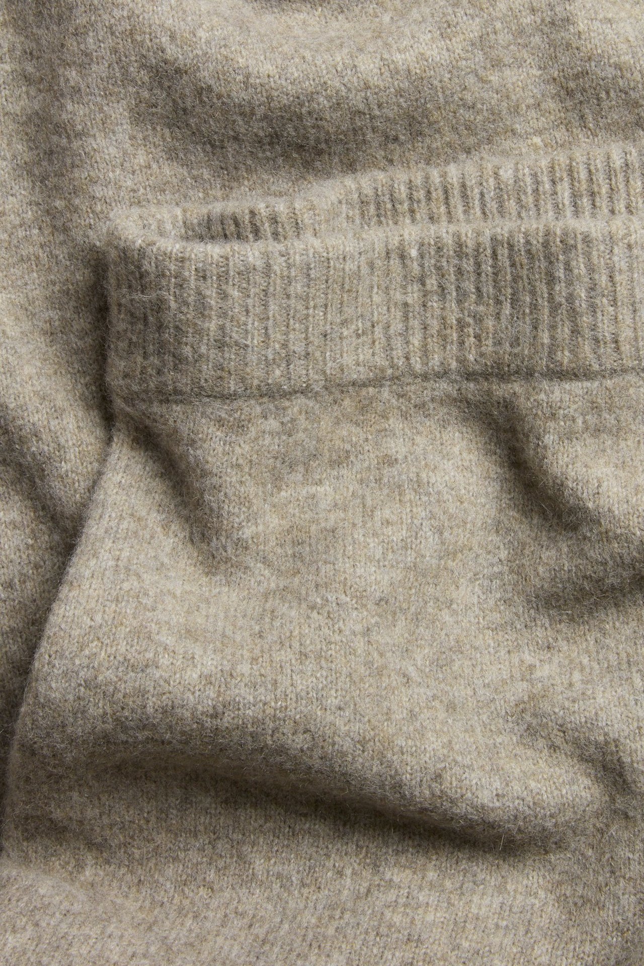 Zbliżenie beżowej melanżowej dzianinowej prostej spódnicy z prążkowanym brzegiem.