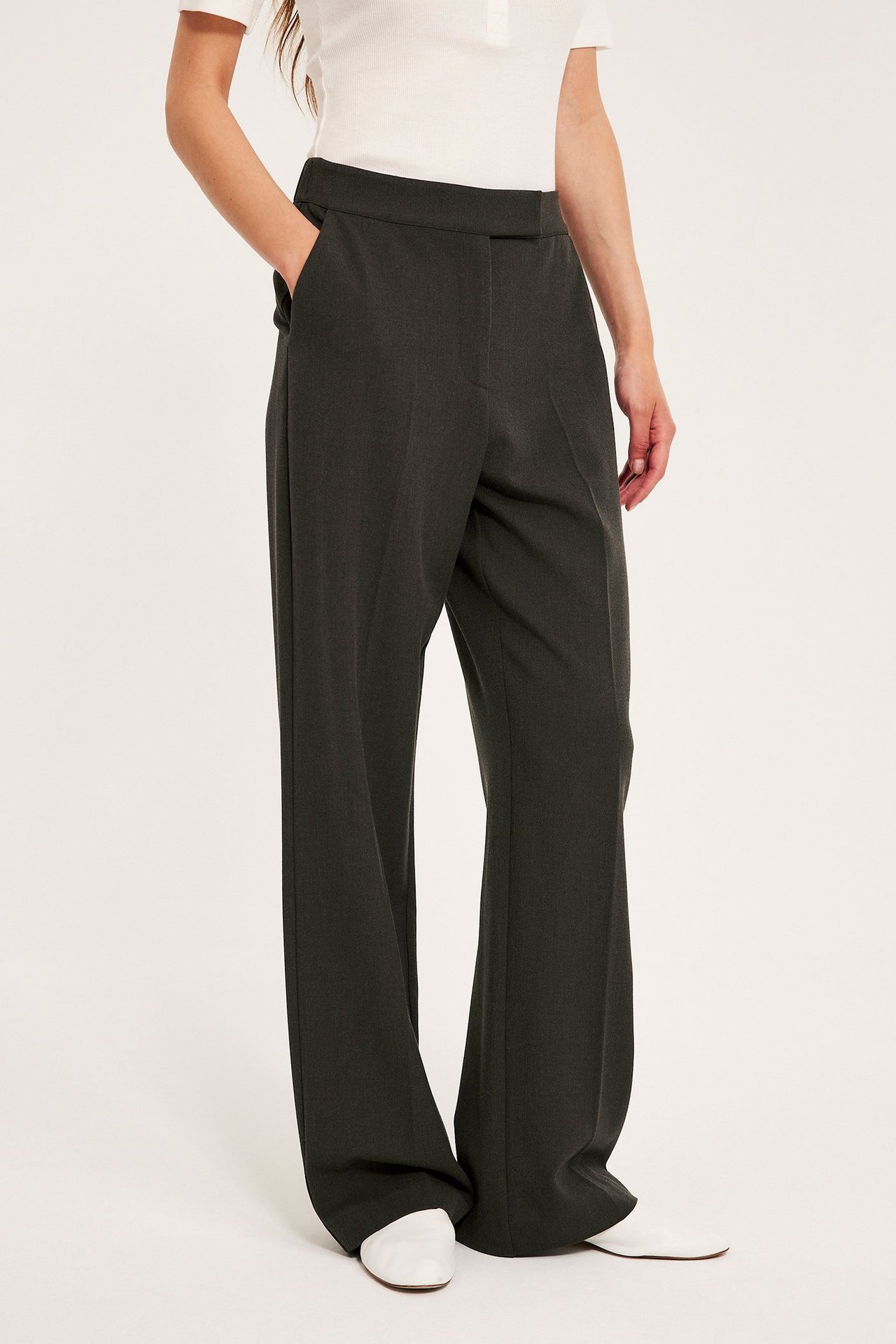 Frontbilde av kvinne i mørkebrune vide dressbukser, en hvit topp og hvite sko.