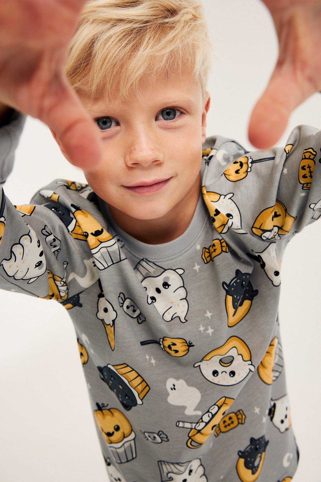 Lähikuva edestä lapsesta, jolla on harmaa, pitkähihainen puuvillainen Halloween-kuvioitu pyjamatoppi.