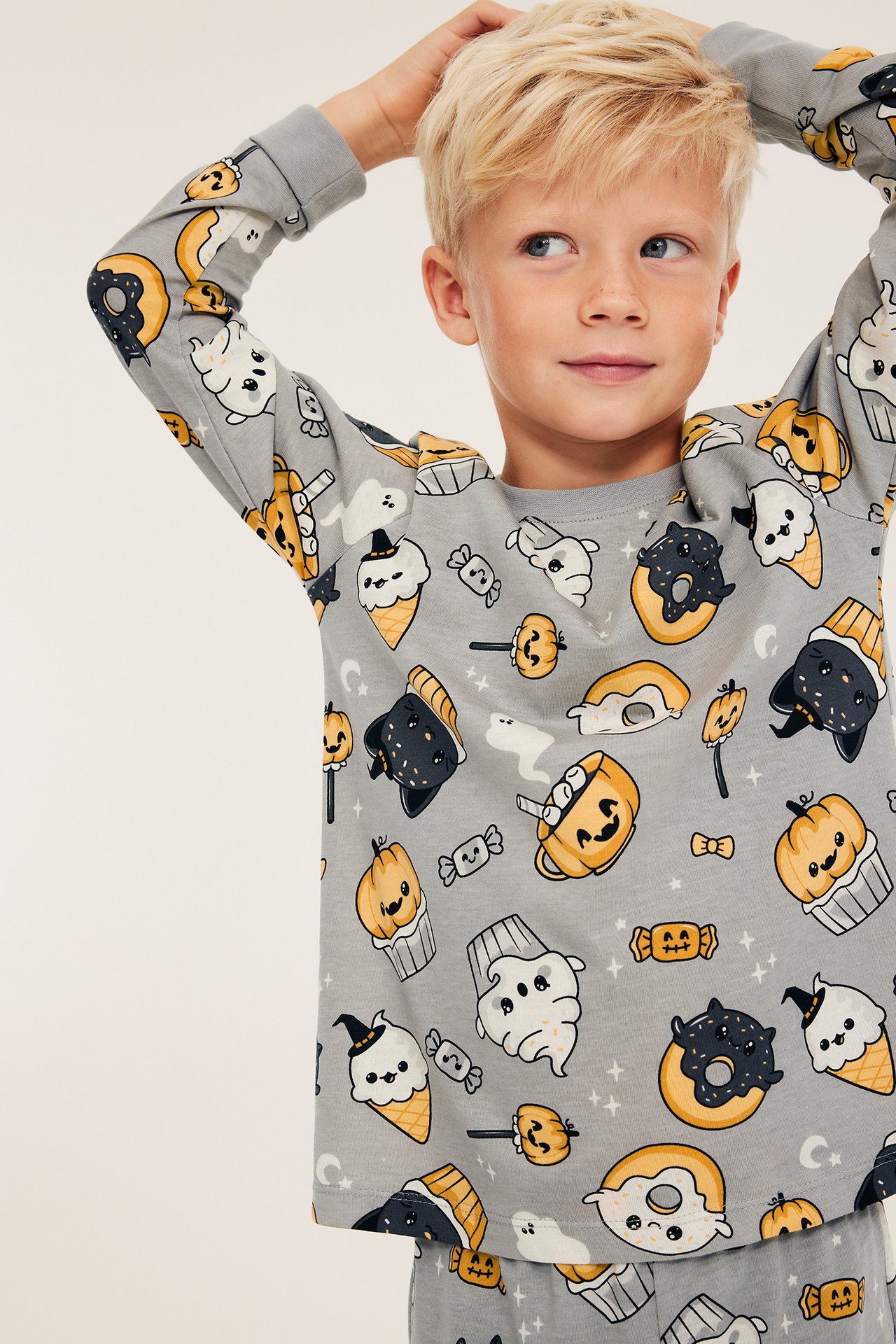 Frontvy: Ett barn bär en grå långärmad pyjamaströja i bomull med halloweenmönster.