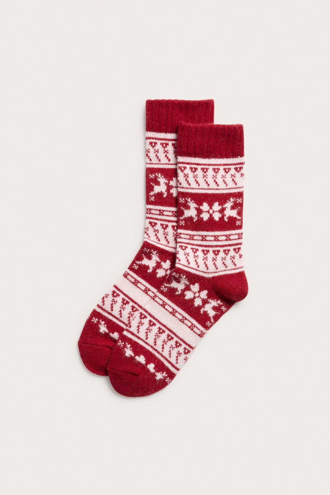Edestä, kaksi punaista jacquard-neulottua sukkaa valkoisilla poro- ja lumihiutalekuvioilla.