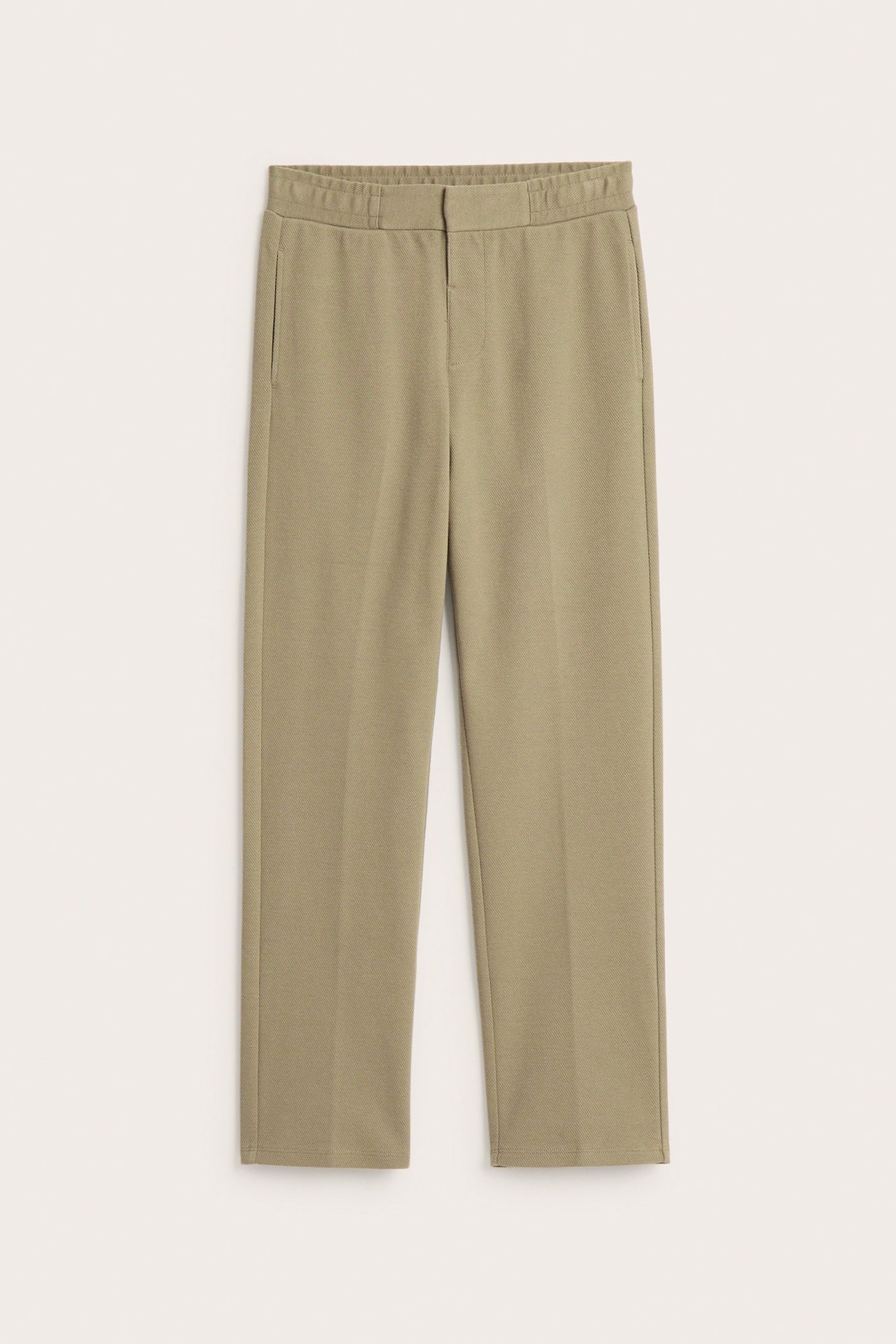 Edestä näkymä tummanbeigestä jerseyhousuista, joissa on prässit, valenappi ja sivutaskut.