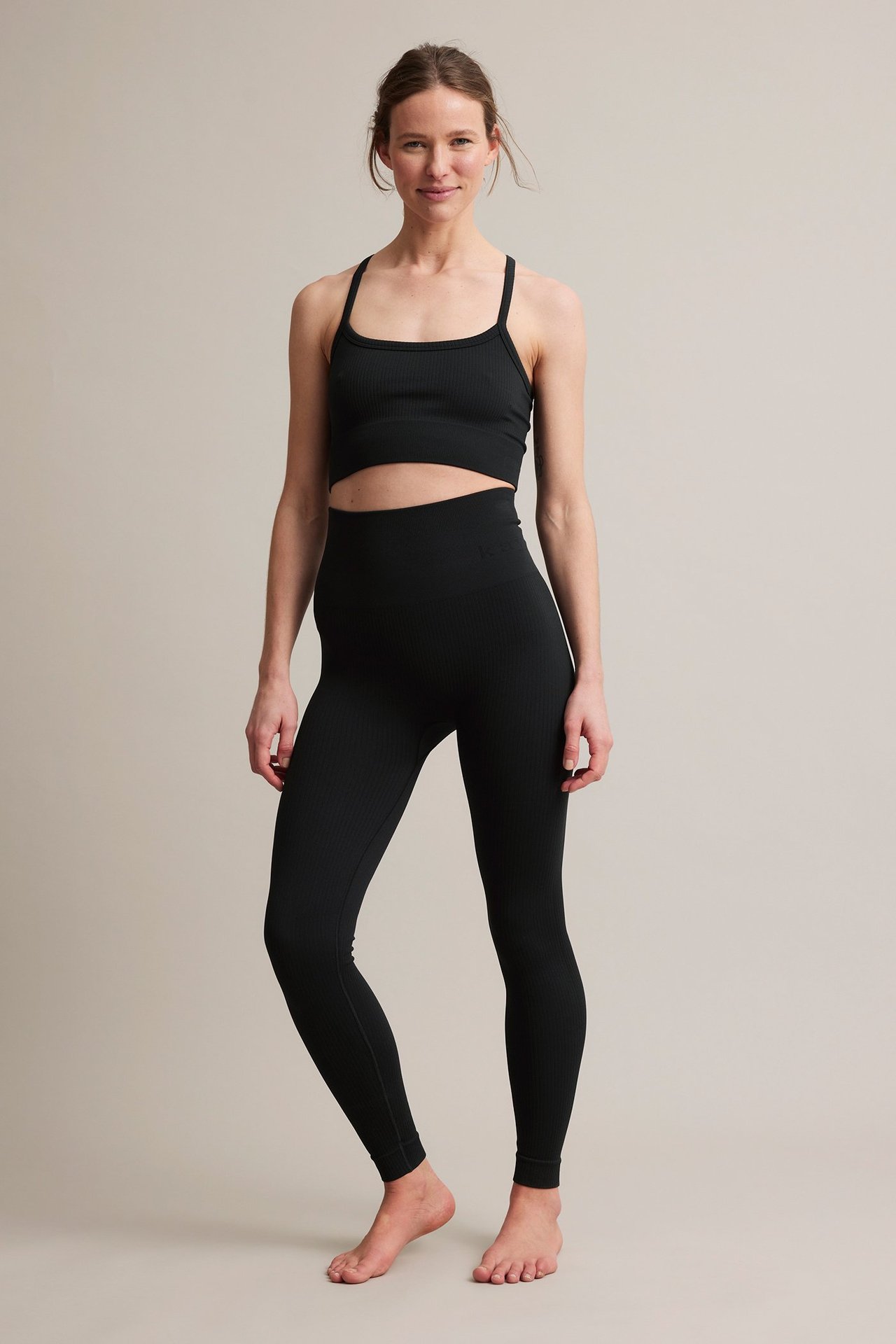 Framifrån: kvinna i svarta ribbade träningstights och matchande svart ribbad sport-bh.