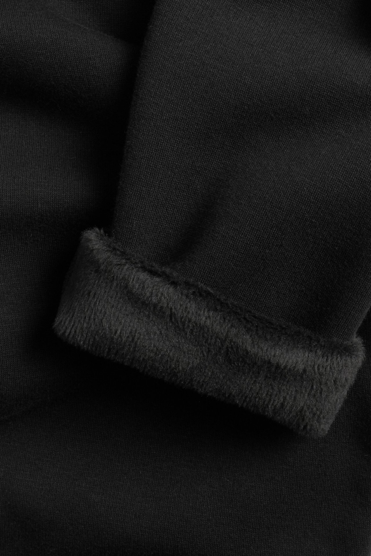Zbliżenie czarnych ocieplanych legginsów z widocznym szczotkowanym, puszystym wnętrzem przy mankiecie.
