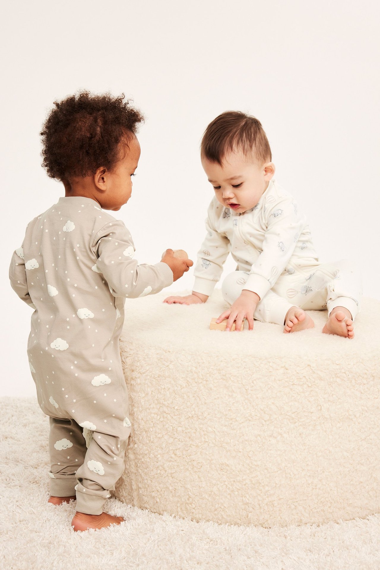 Forfra/side av to babyer i mønstrede pysjamaser: en offwhite med glidelås foran, en lys grå med glidelås bak.