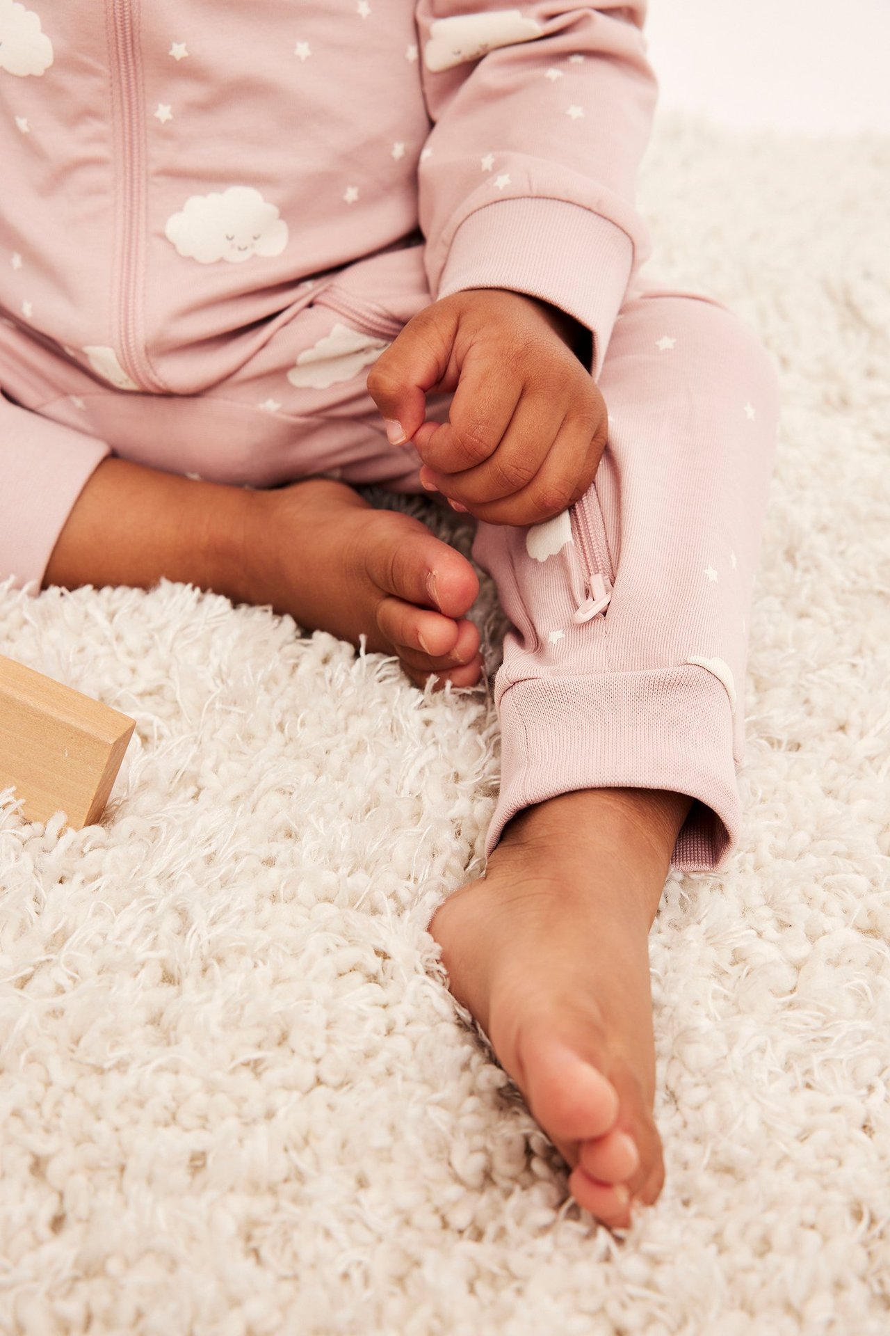 Lähikuva vauvasta vaaleanpunaisessa pitkähihaisessa potkupuvussa, pilvi- ja tähtikuvio, kaksisuuntainen vetoketju.