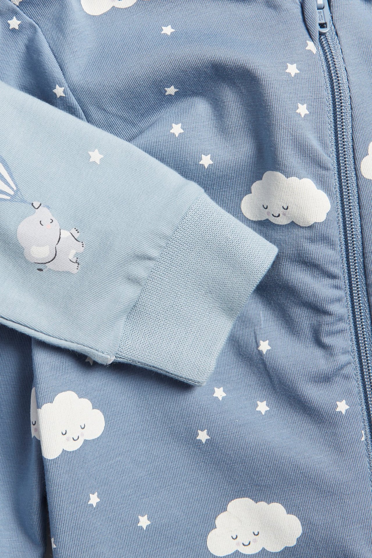Zbliżenie niebieskiego wzorzystego pajacyka niemowlęcego z białymi chmurami, gwiazdami i nadrukiem słonia, z zamkiem.