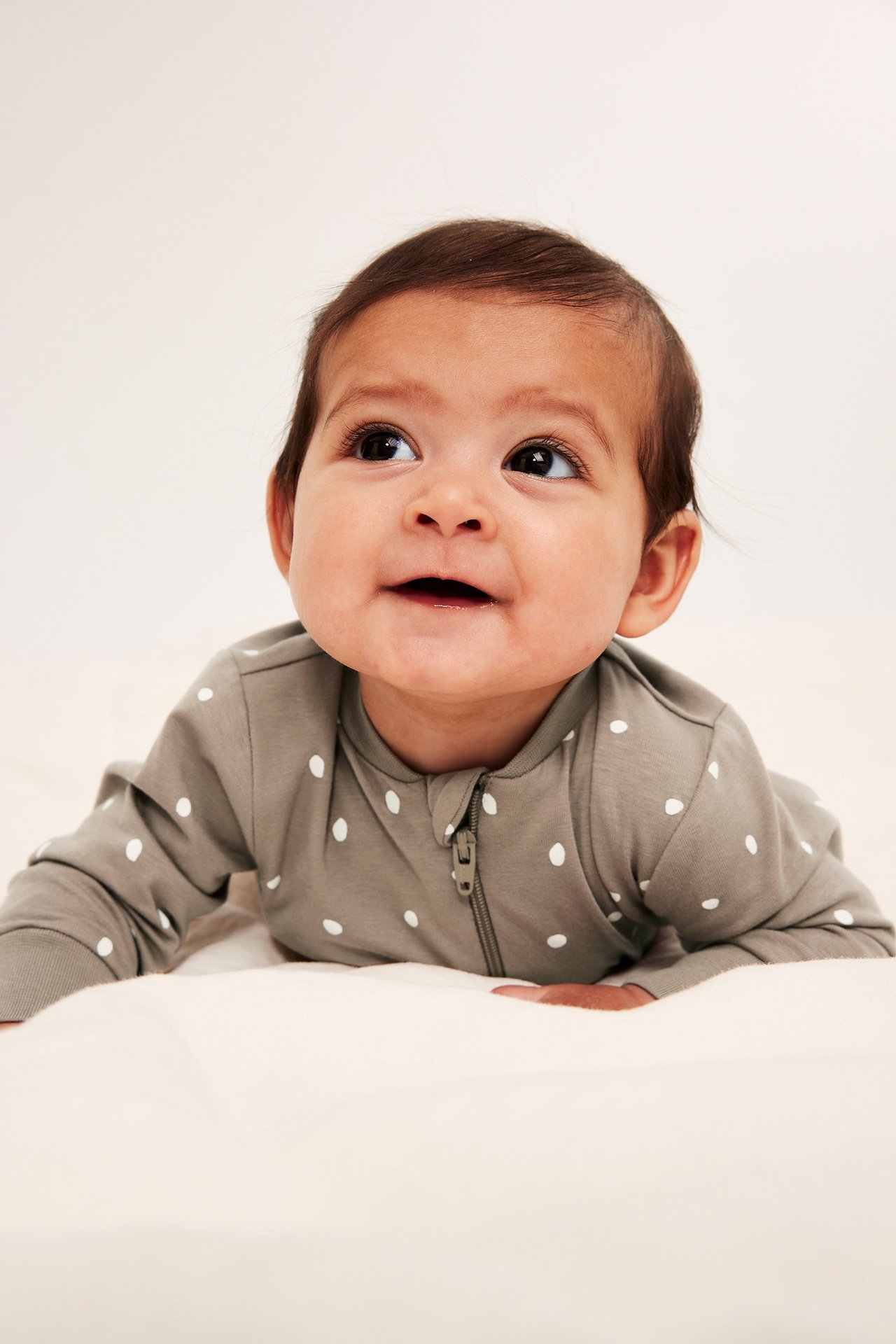 Frontvy av en baby i beige prickig pyjamas med dragkedja fram.
