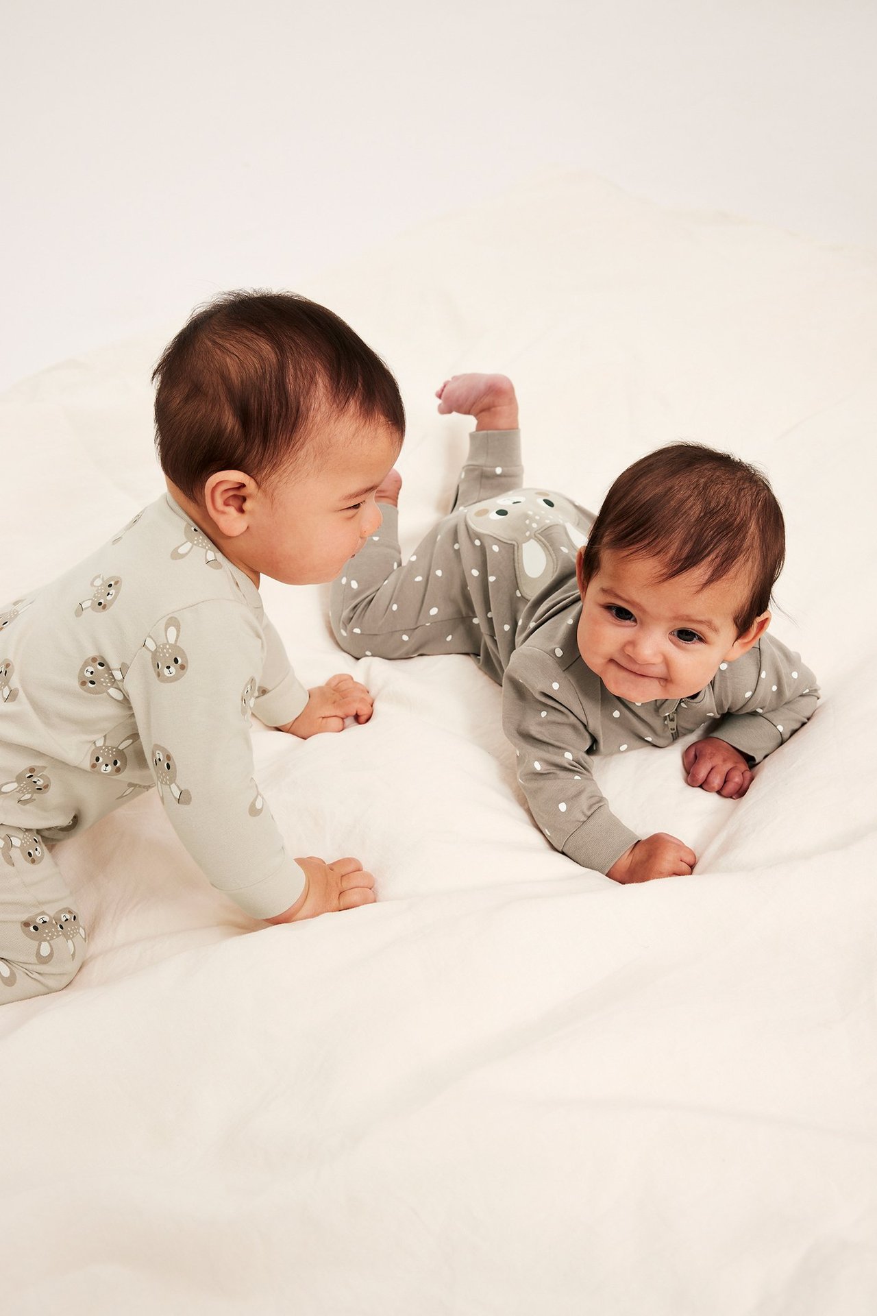 Frontvy: Två bebisar i pyjamasar. En beige med kanintryck, en grå med prickar och applikation baktill.