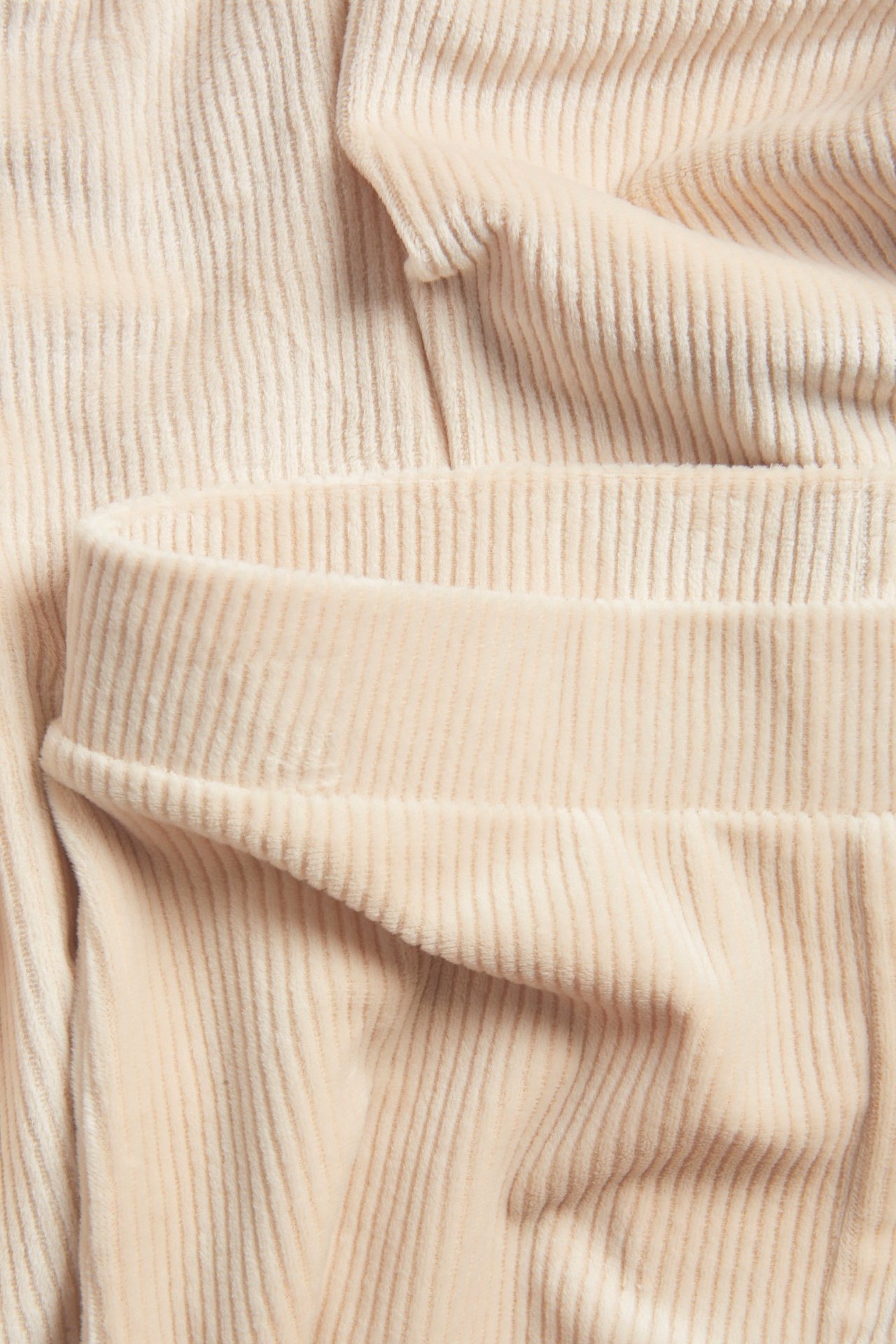 Zbliżenie beżowych prążkowanych welurowych legginsów, ukazujące fakturę materiału i pas.