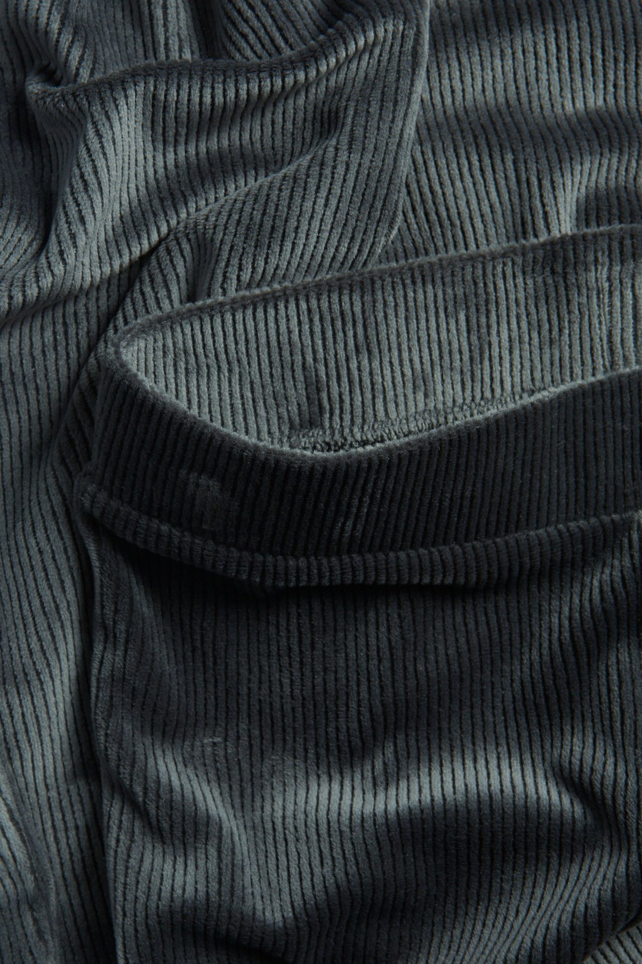 Zbliżenie czarnych prążkowanych welurowych legginsów, ukazujące fakturę materiału i pas.