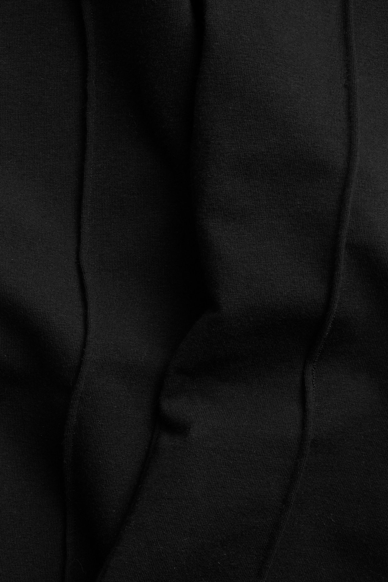 Zbliżenie czarnych, rozszerzanych spodni dresowych z zaprasowanymi kantami.