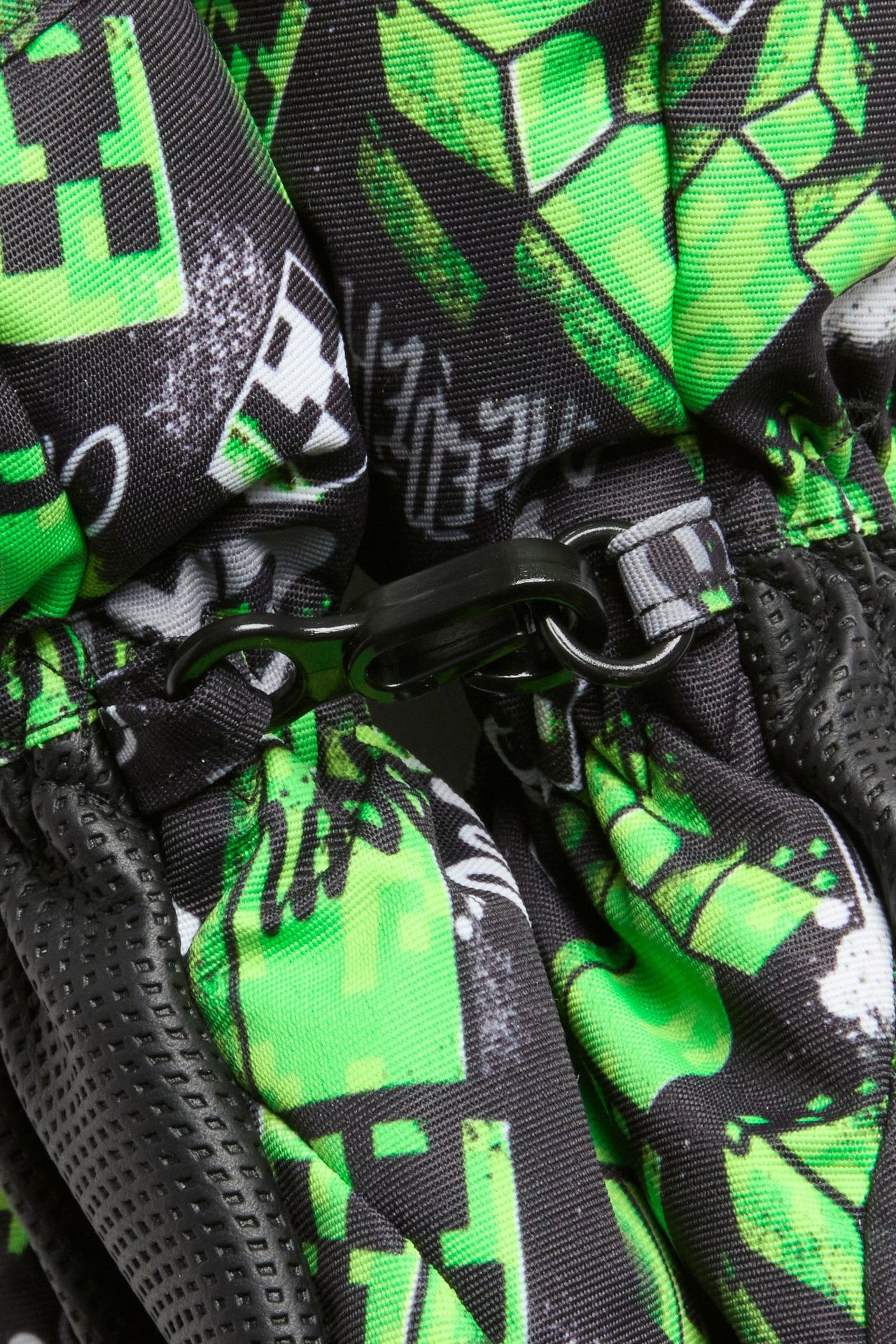 Lähikuva mustista ja vihreistä kuvioiduista lasten Minecraft-hiihtorukkasista mustalla kiinnitysklipsillä.