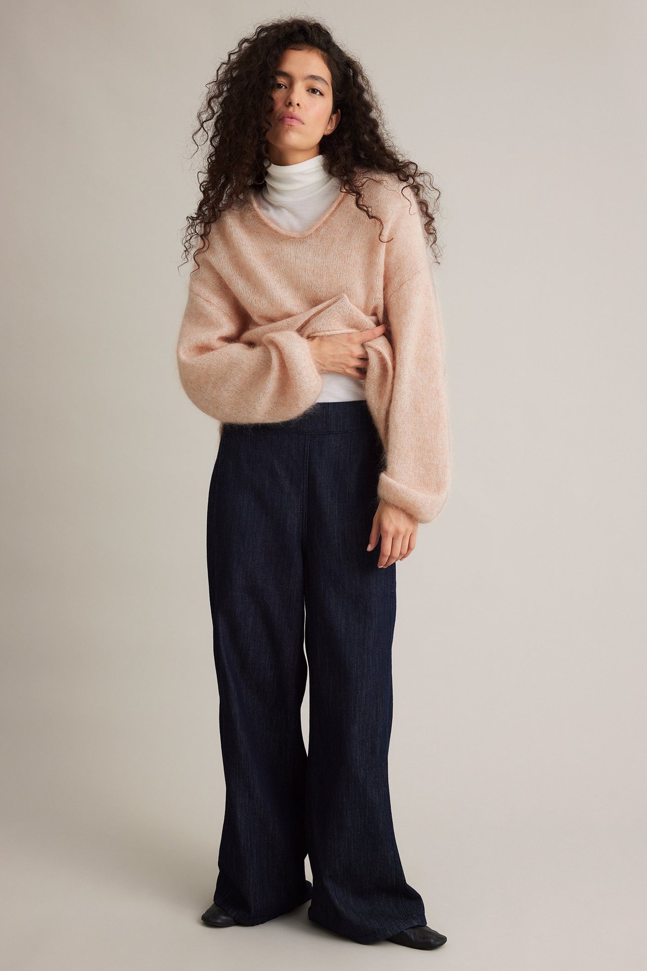 Frontbilde av kvinne i oversized lys rosa mohairgenser, hvit turtleneck og mørkeblå vide bukser.
