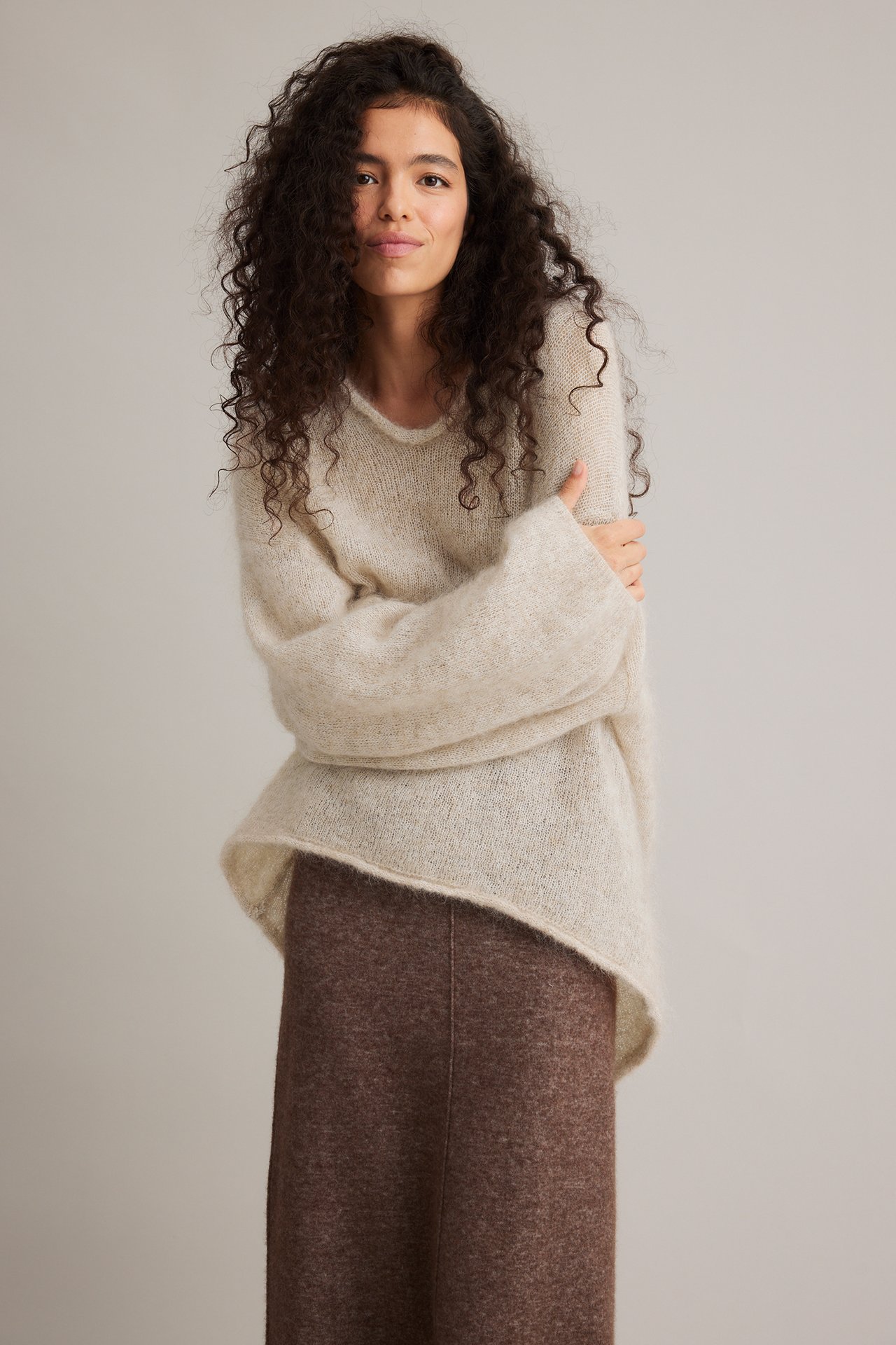 Front view: Kvinne i en lys beige mohairblanding strikket genser med vide ermer, brun skjørt.