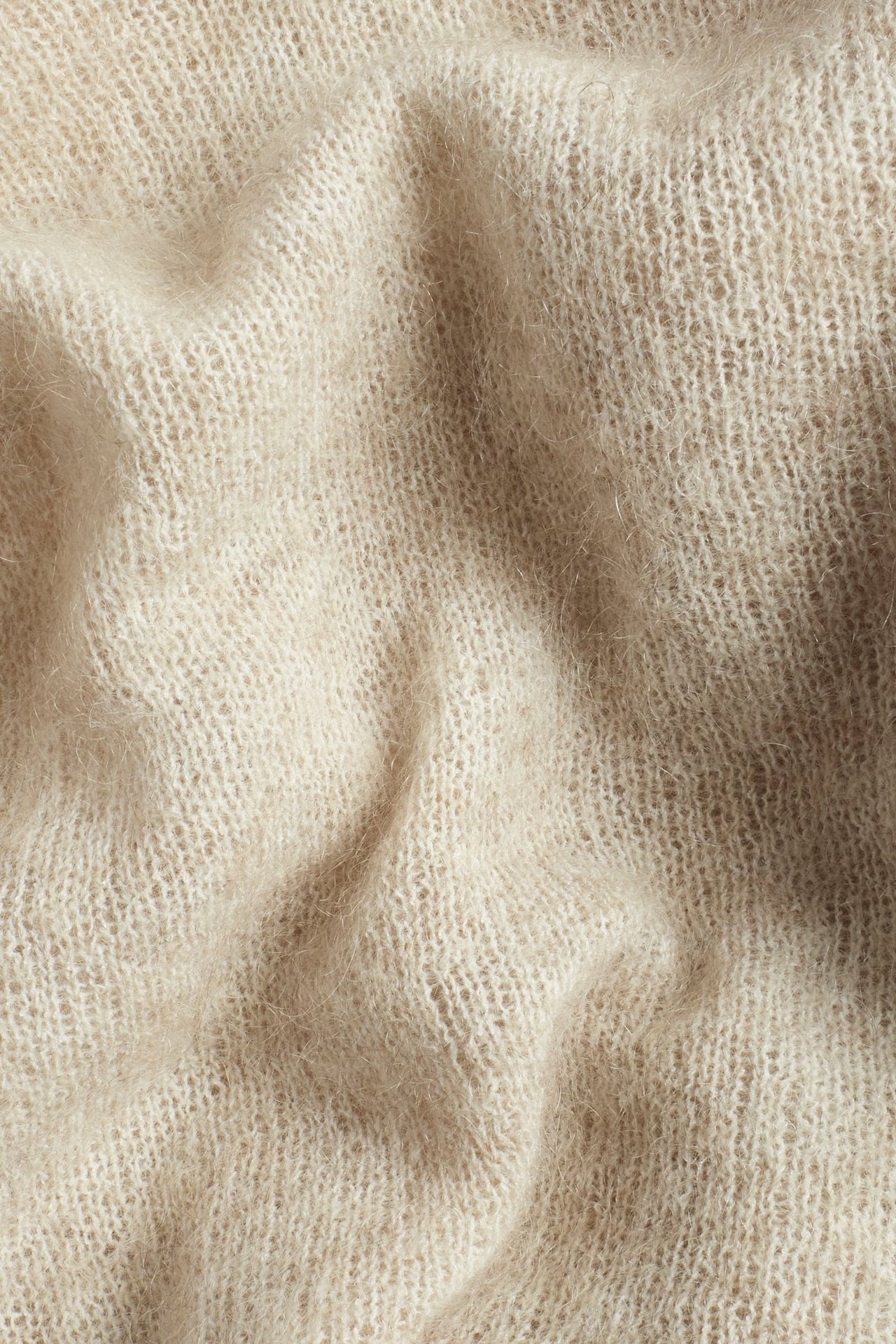 Zbliżenie jasnobeżowej dzianiny z mieszanki moheru o jednolitym wzorze.