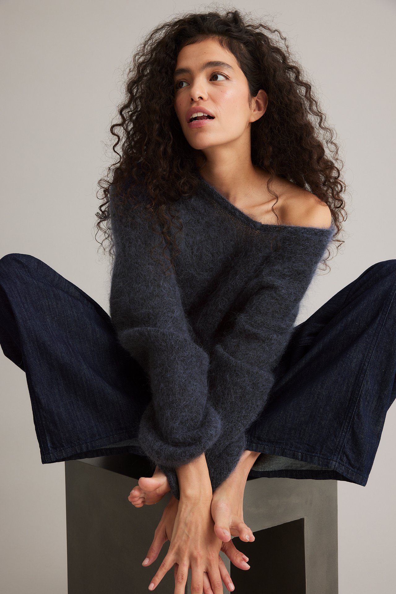 Forfra: kvinne i mørkeblå lodden off-shoulder mohairblanding genser og mørkeblå vide jeans.