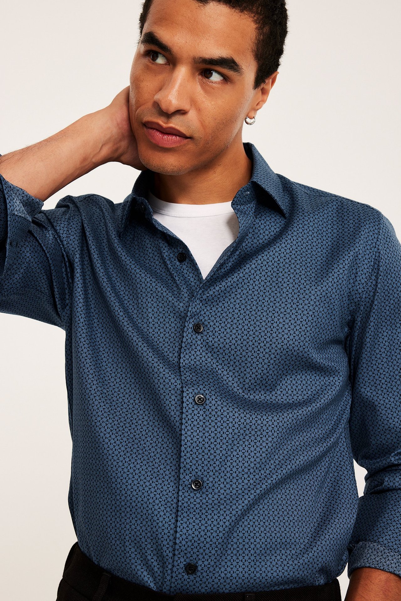 Närbild framifrån på en man i en blåmönstrad bomullsskjorta över en vit t-shirt.