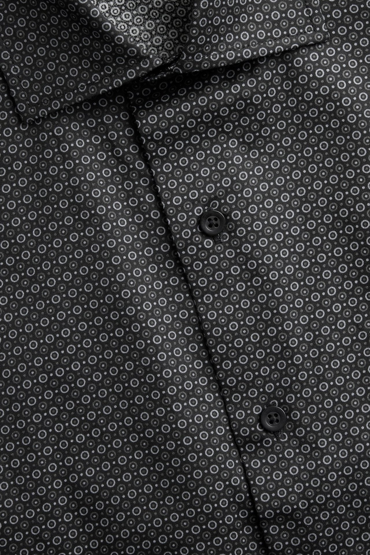 Zbliżenie z przodu na czarną, bawełnianą koszulę męską z drobnym okrągłym wzorem i czarnymi guzikami.