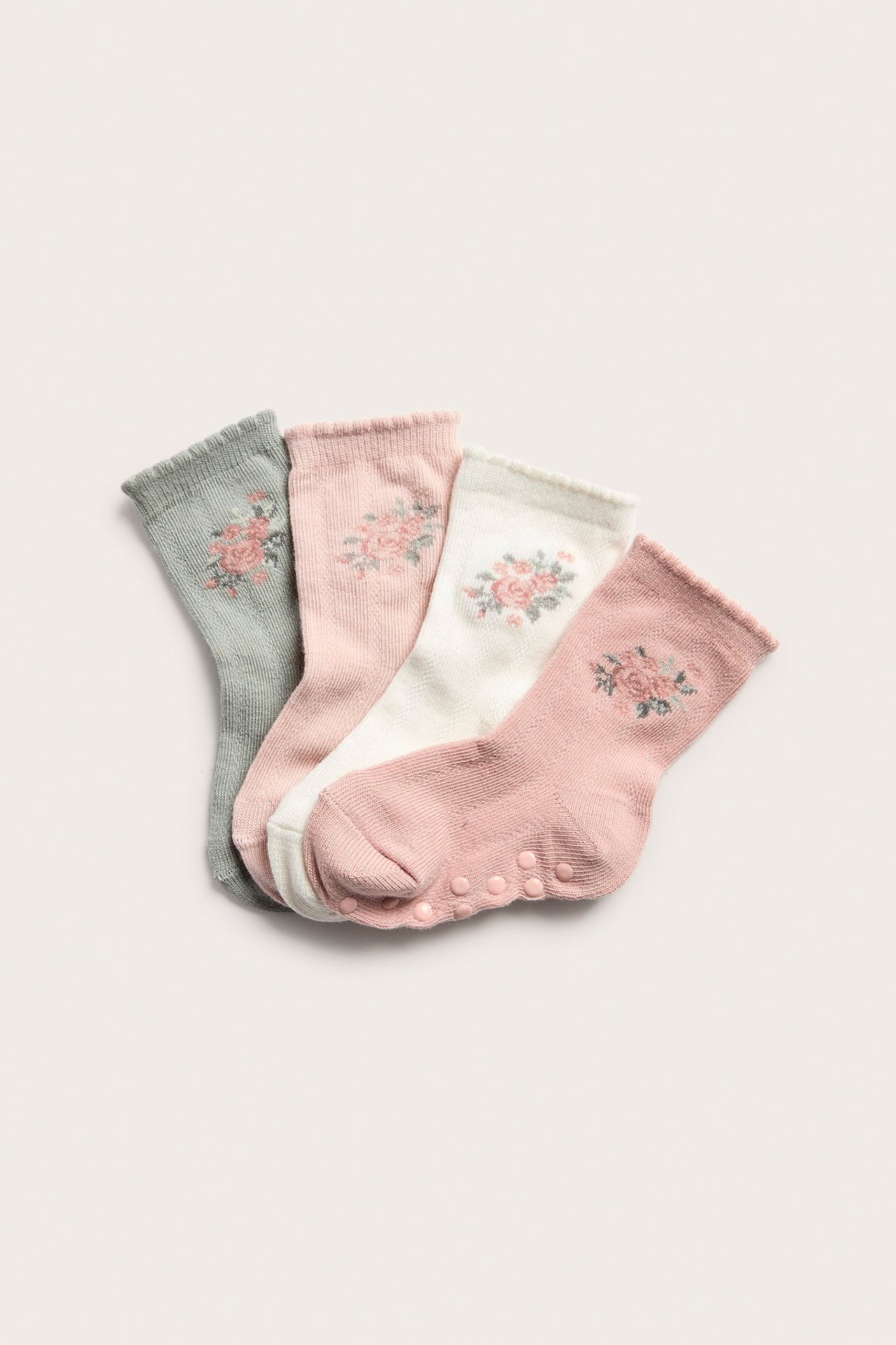 Ovenfra: Fire strukturstrikkede babystrømper i lys rosa, hvit, grå og gammelrosa, med blomsterbroderi. Ett par har antiskli.